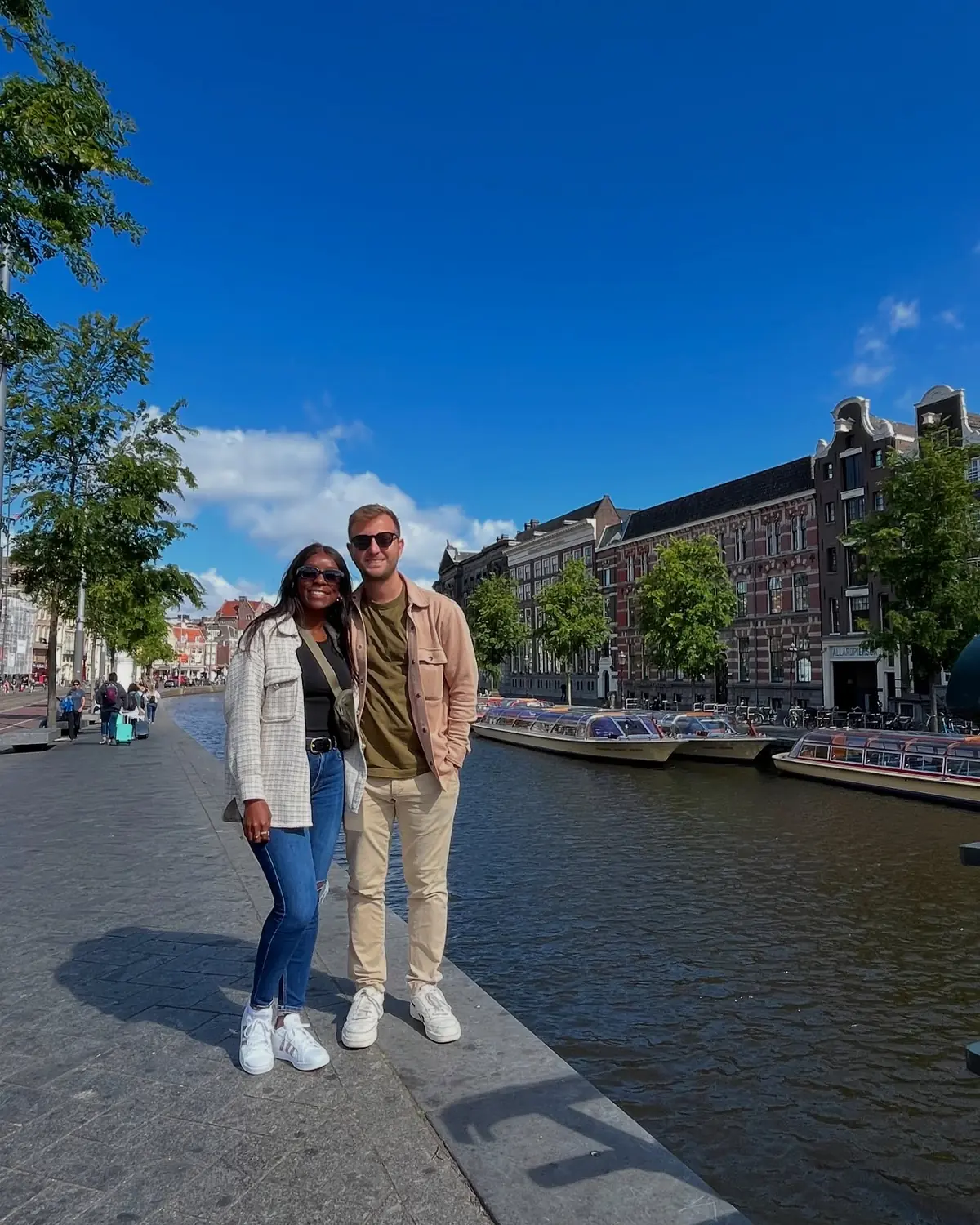Us on a sunny canal-side in Amsterdam with tour boats moored behind