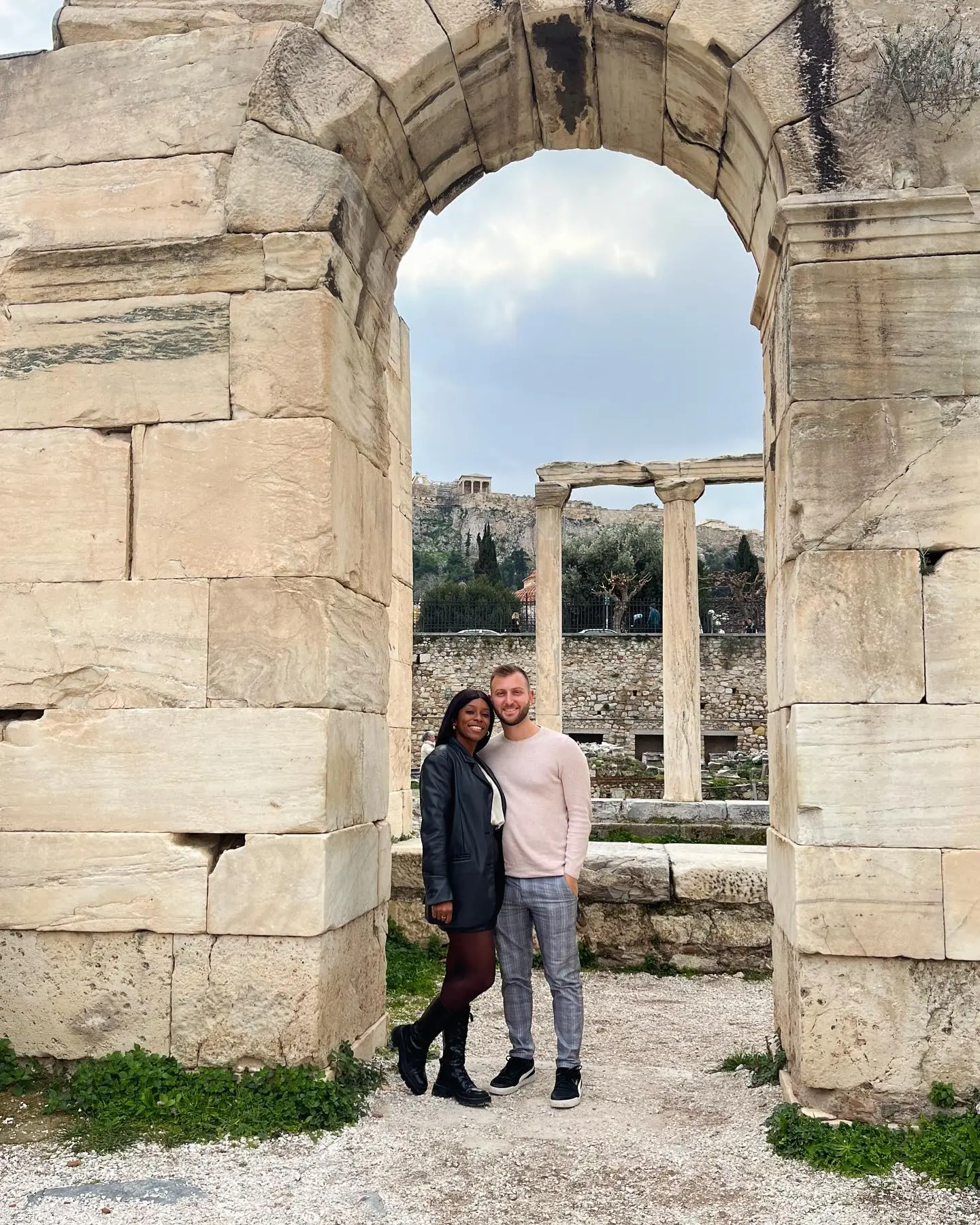 Us framed by a stone arch with the Acropolis beyond