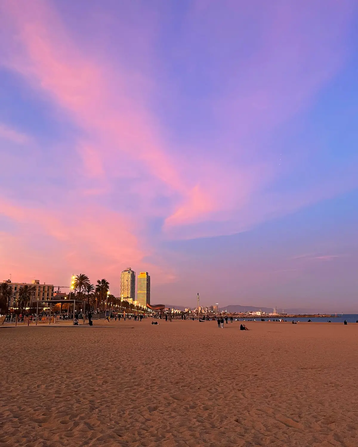 Barceloneta beach at sunset with a pink and purple sky over the sand and sea
