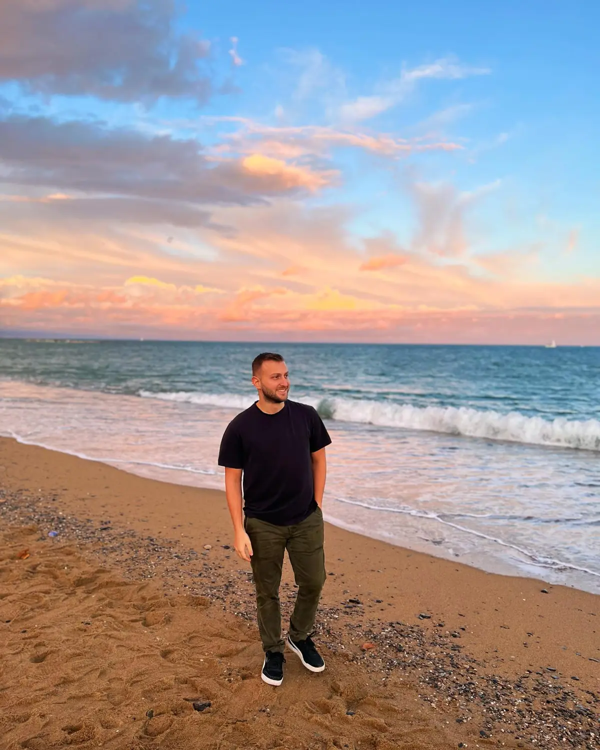 Andrew on the beach at sunset with waves rolling in behind him in Barcelona