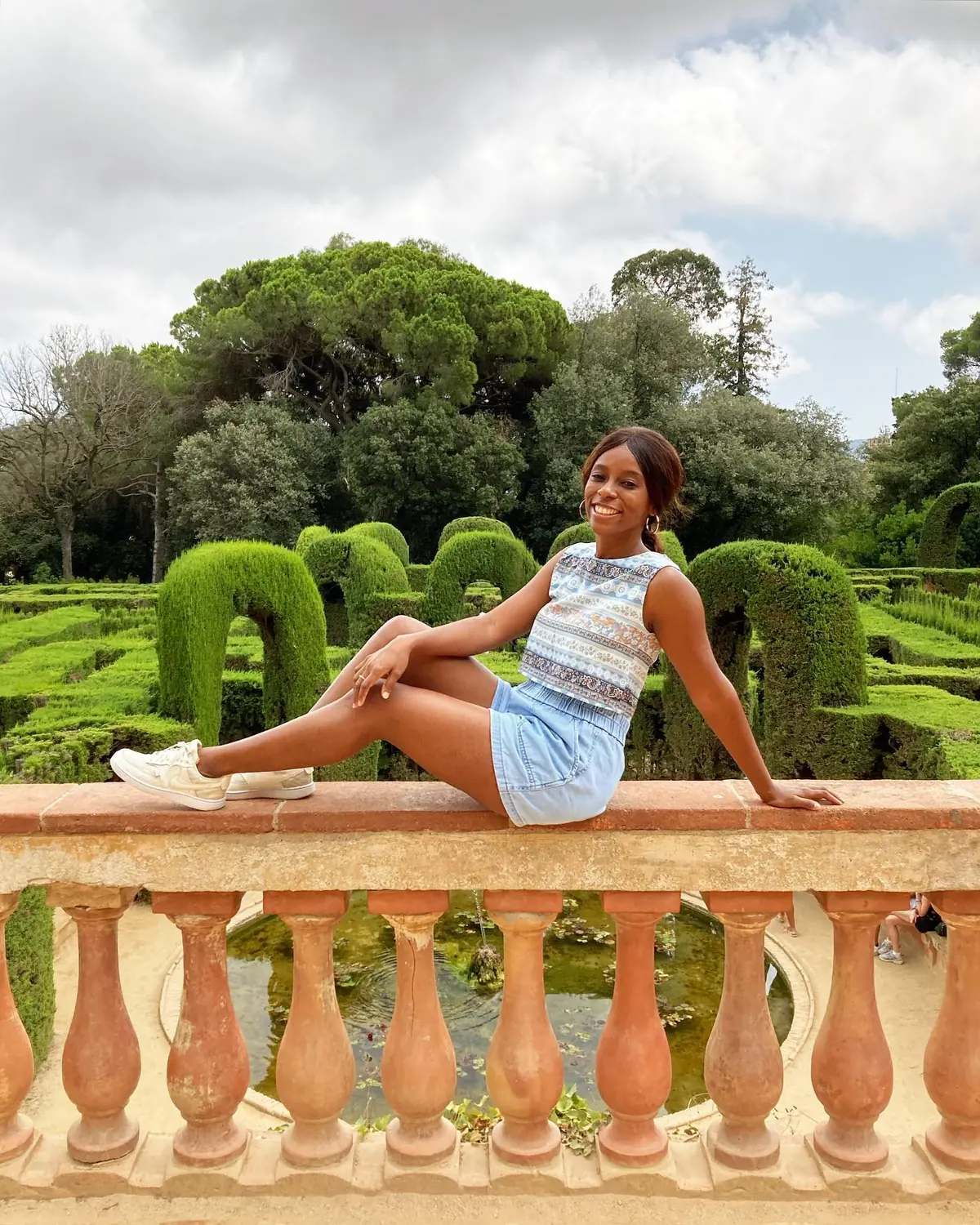 Melody sitting on a balustrade in front of the hedge maze at Parc del Laberint d'Horta