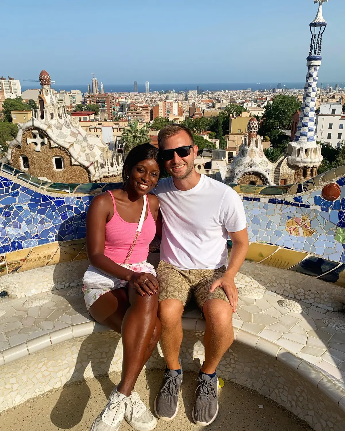 Us on the mosaic serpentine bench at Park Güell with the Barcelona skyline and sea behind