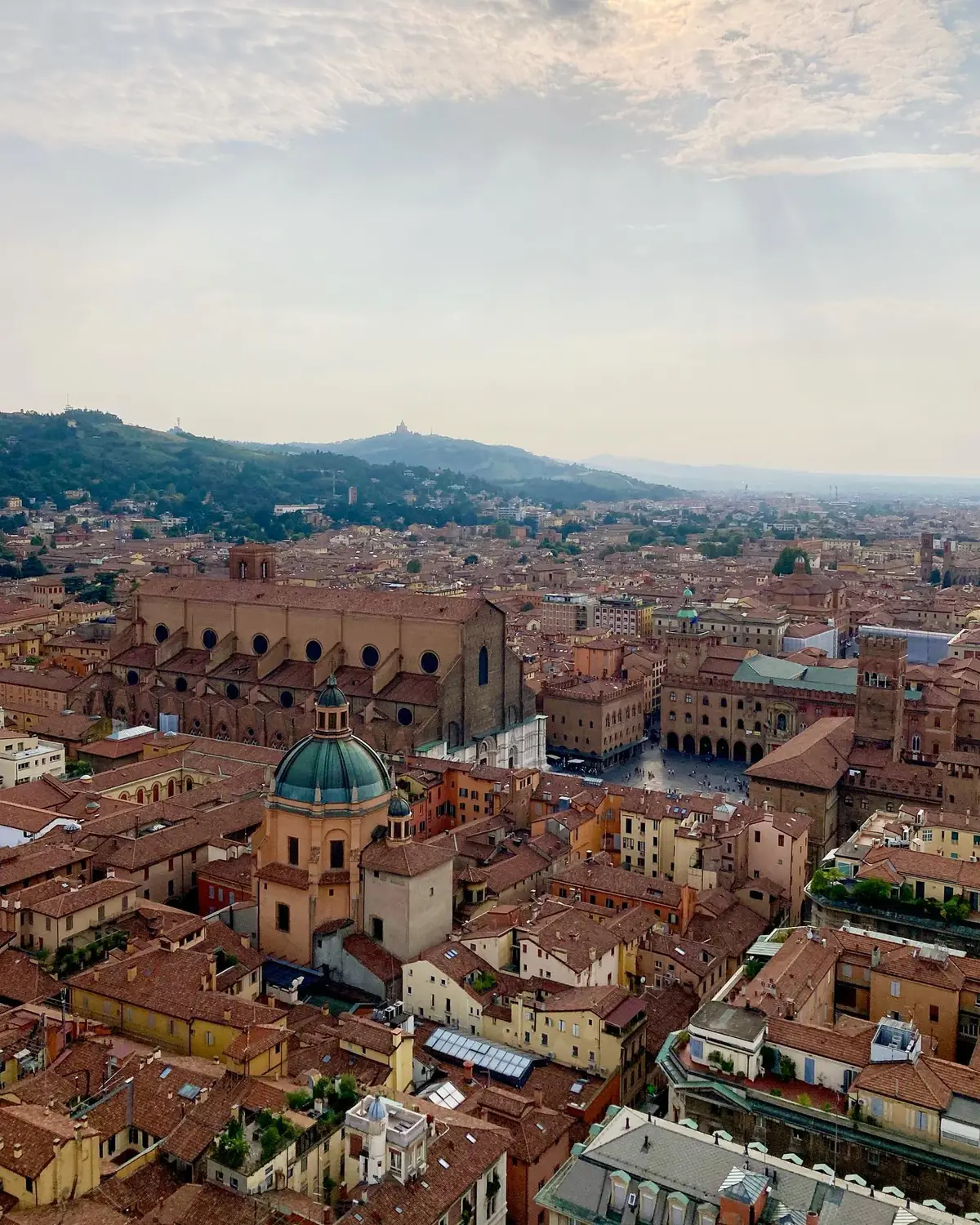 Aerial view over Bologna's red rooftops with San Petronio and the San Luca sanctuary on the hill
