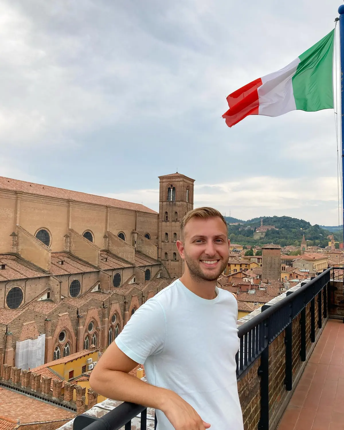 Andrew on a rooftop terrace over Bologna with an Italian flag and the hills behind