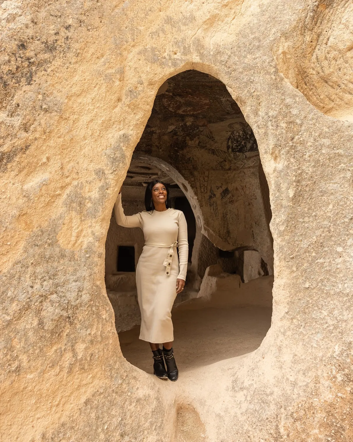 Melody framed in a carved cave-church arch with faded Byzantine frescoes behind