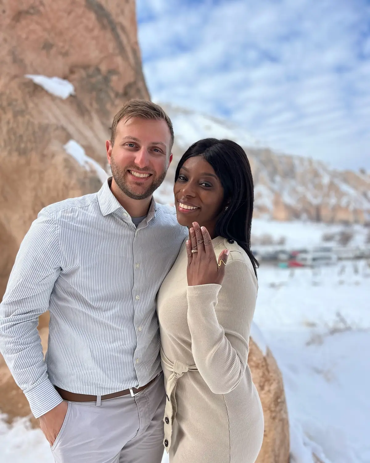 Melody smiling and showing off her engagement ring beside Andrew, snowy Cappadocia behind
