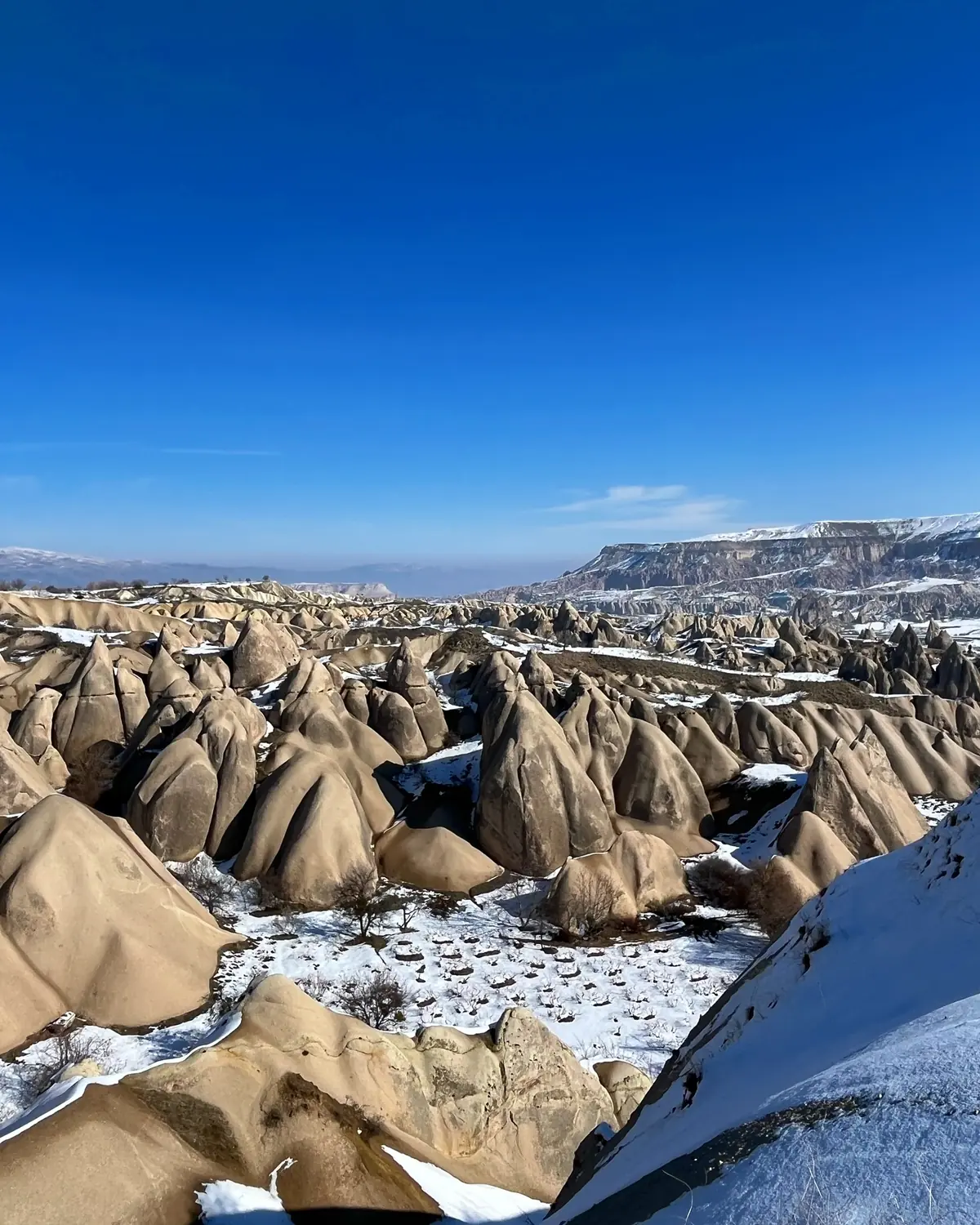 A snow-dusted valley of countless fairy chimneys under a bright blue Cappadocia sky
