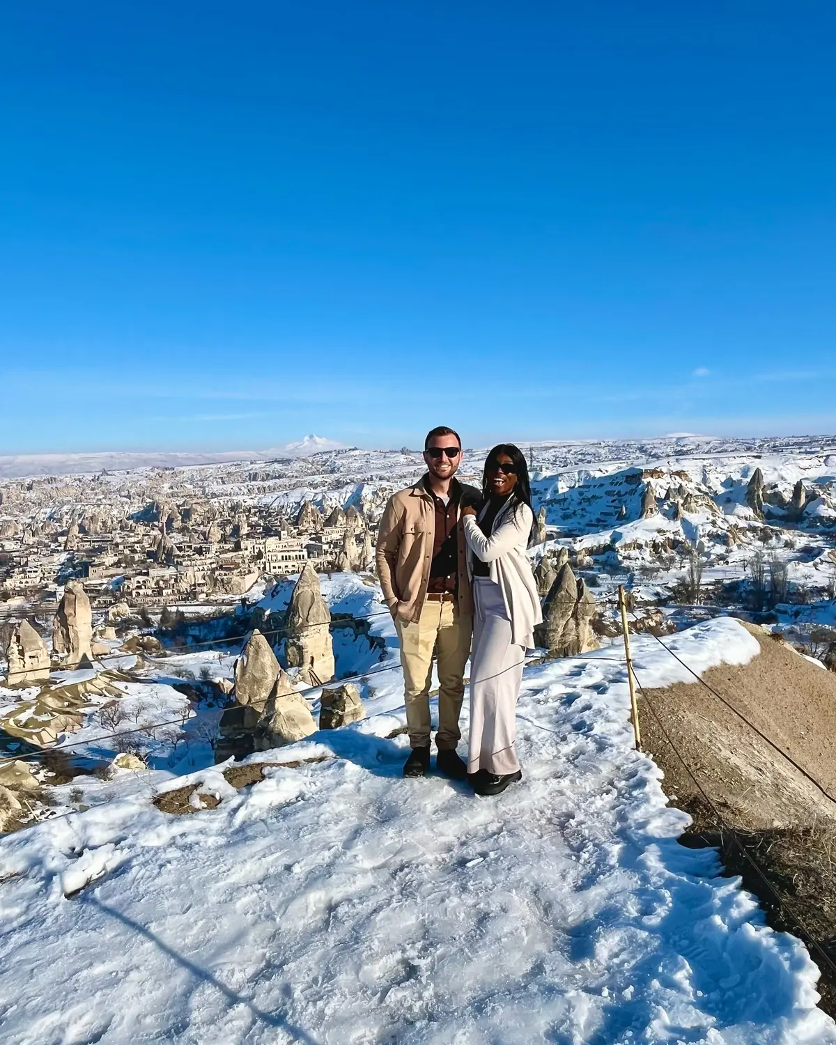 Us on a snowy hilltop with the whole Göreme valley of fairy chimneys spread out behind