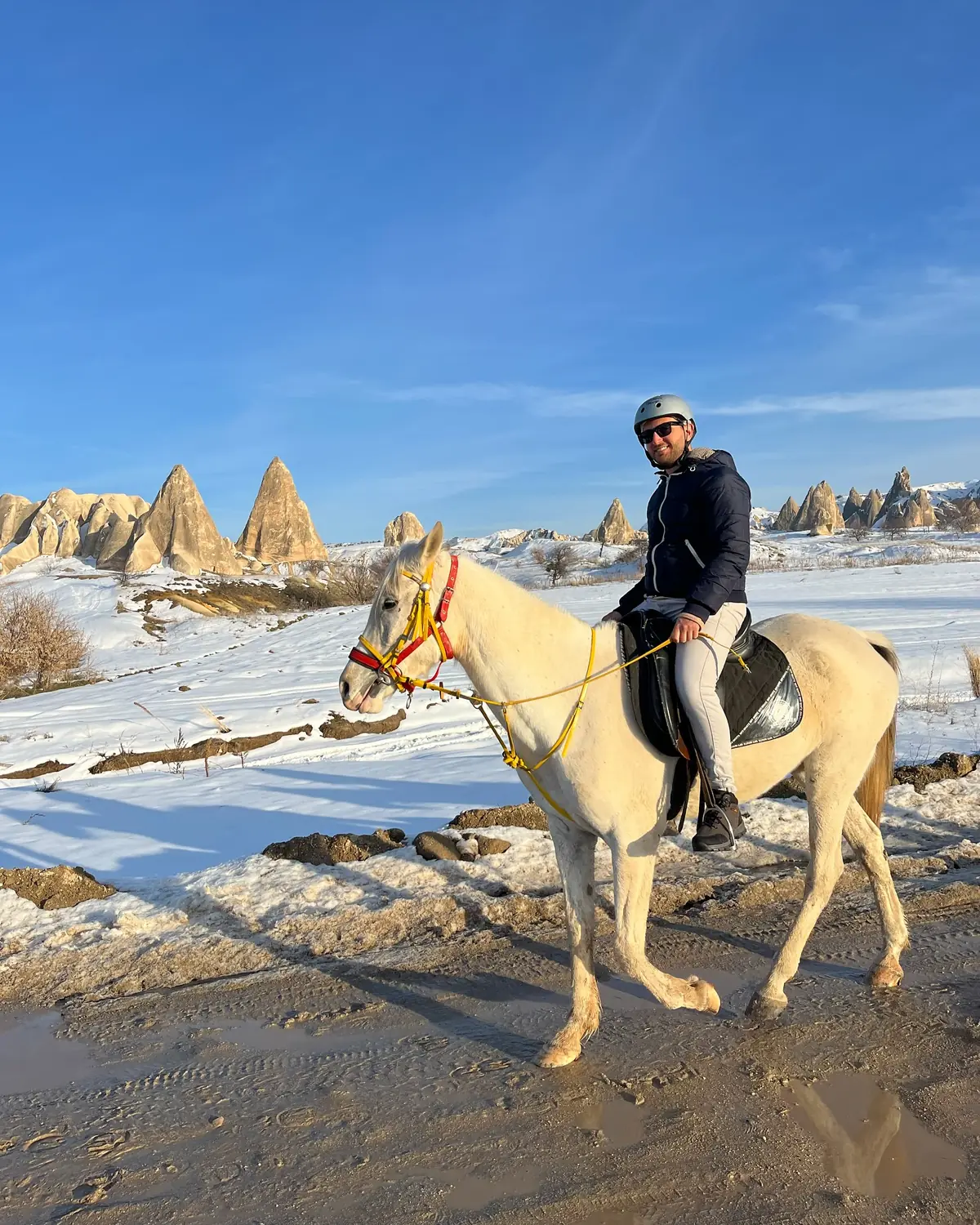 Andrew riding a white horse through the snow with fairy chimneys behind