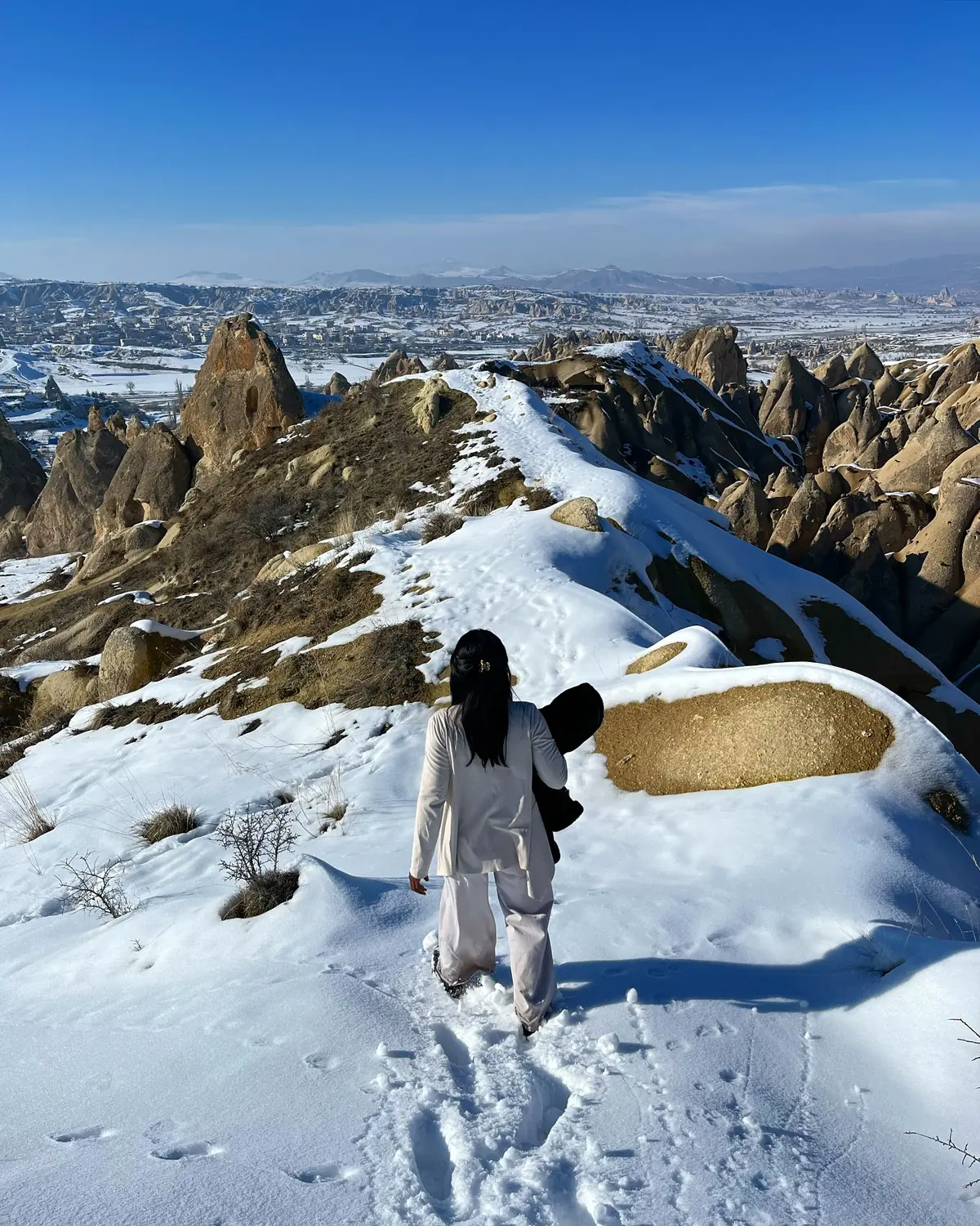 Melody walking down a snowy ridge trail with the Cappadocia valley opening up ahead