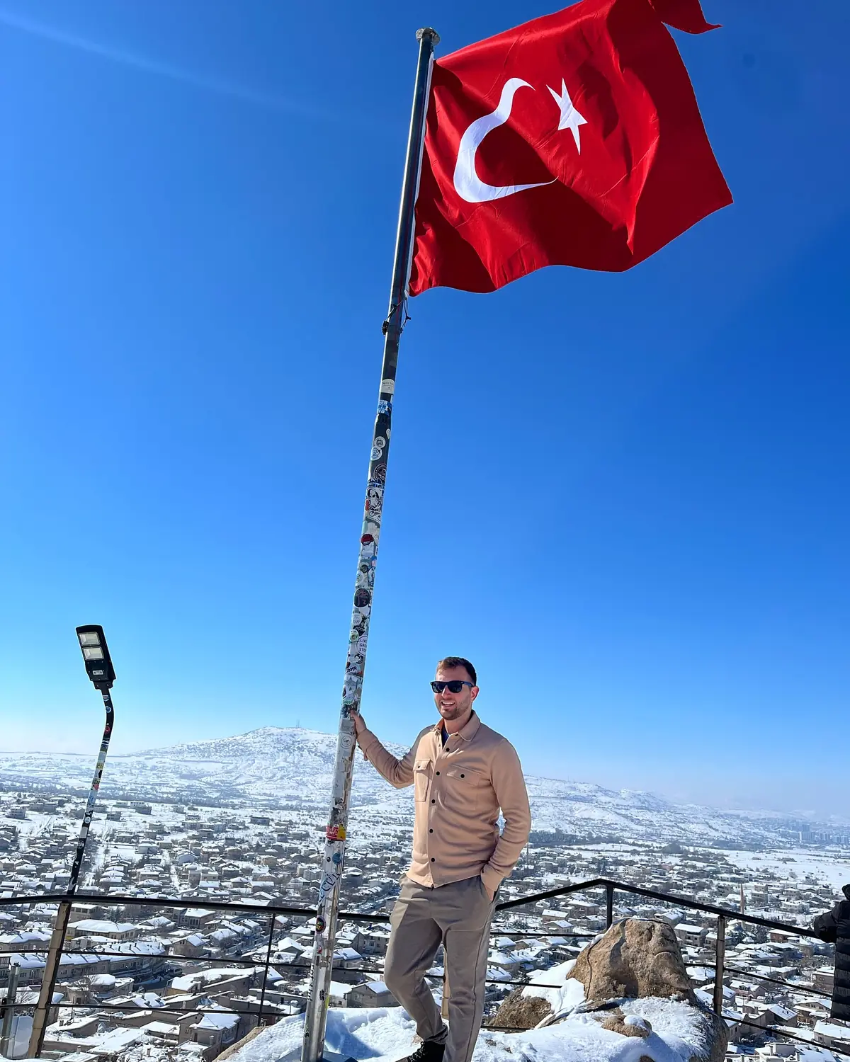 Andrew holding a tall Turkish flagpole at a viewpoint high above a snowy town