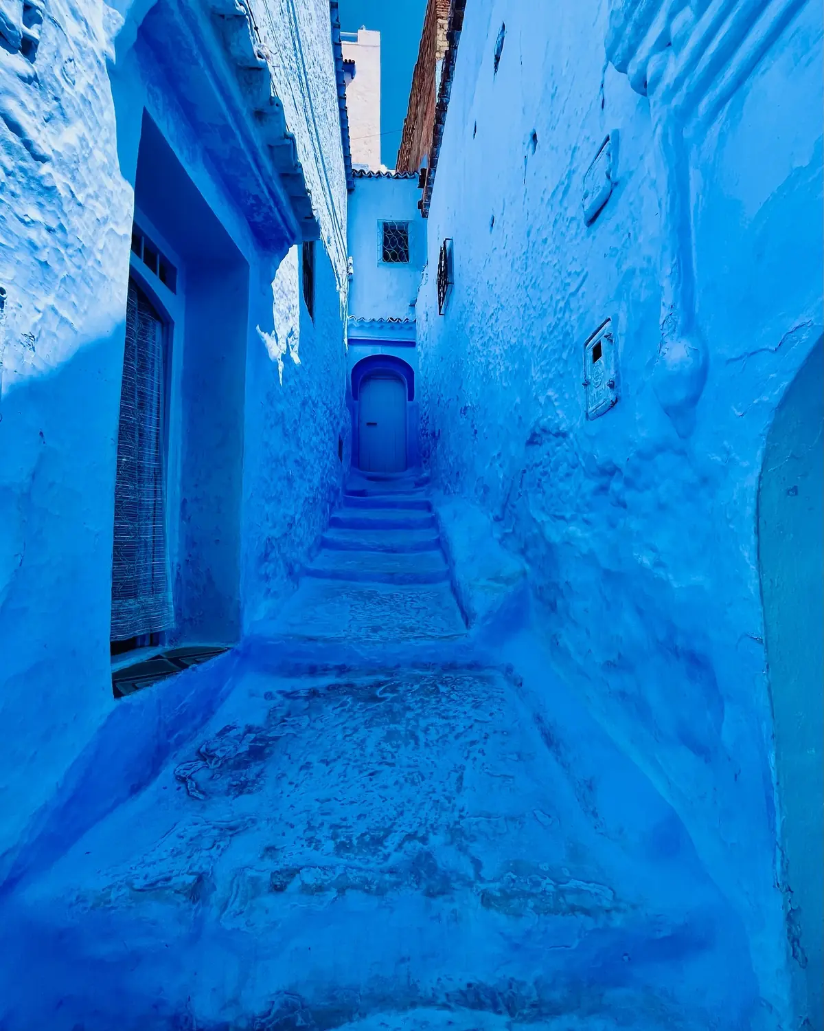 A narrow blue-washed alley of steps leading to a small blue door in Chefchaouen