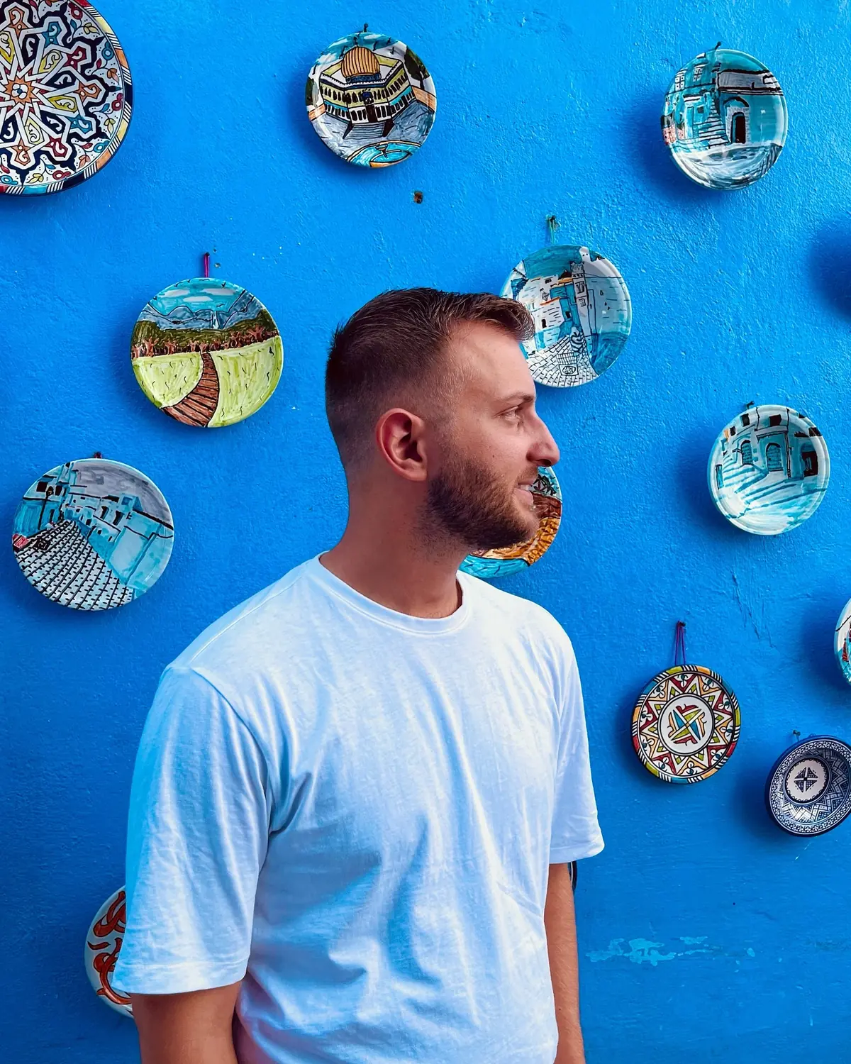 Andrew against a blue Chefchaouen wall hung with painted plates