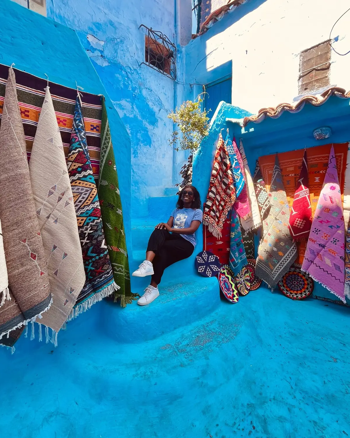 Melody among hanging Berber rugs in a blue Chefchaouen lane