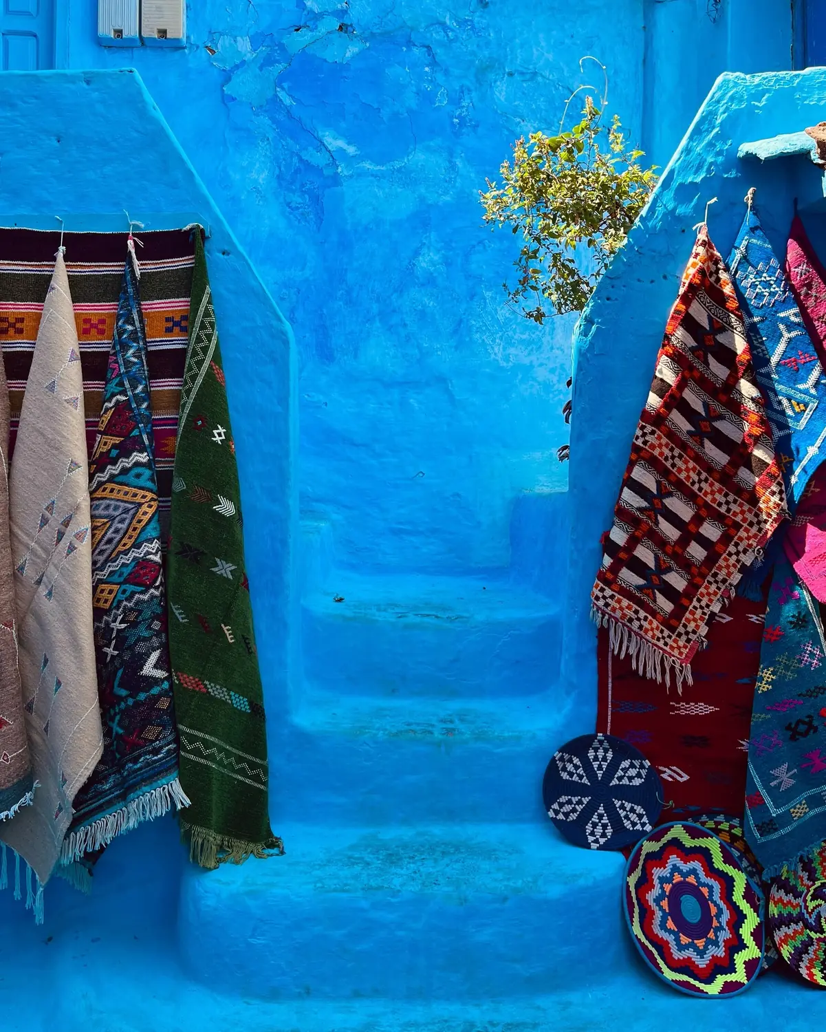 Handwoven rugs and woven discs displayed on blue steps in Chefchaouen
