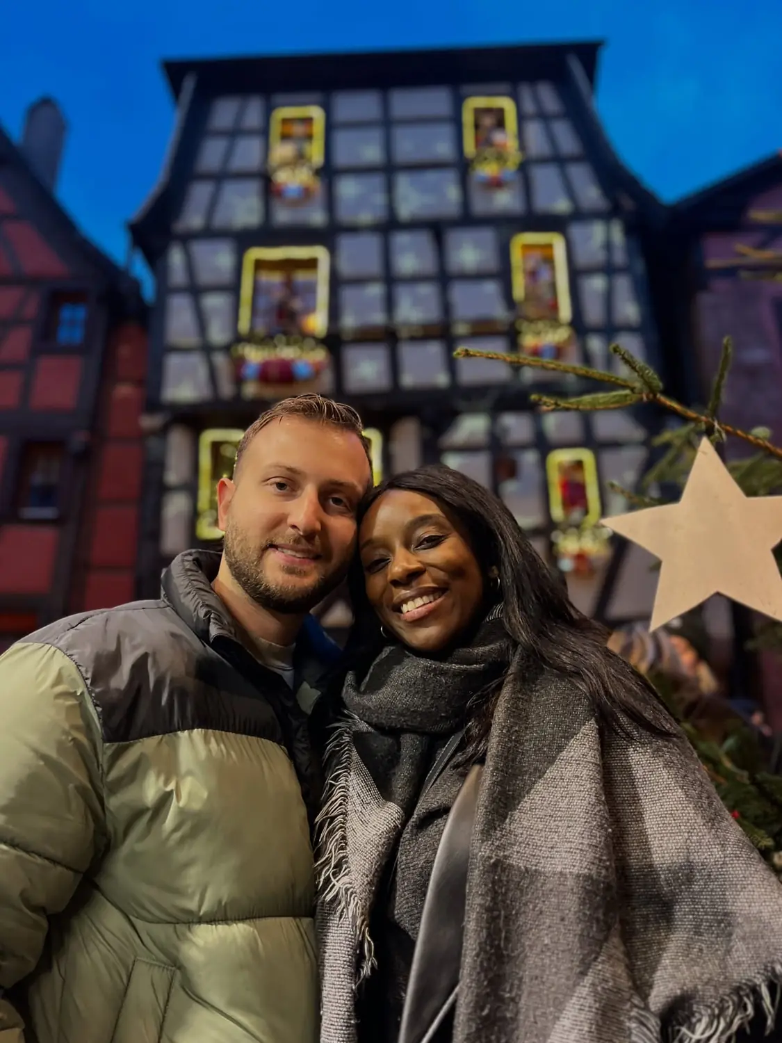 A night selfie of us in front of a Colmar house lit up as a giant advent calendar