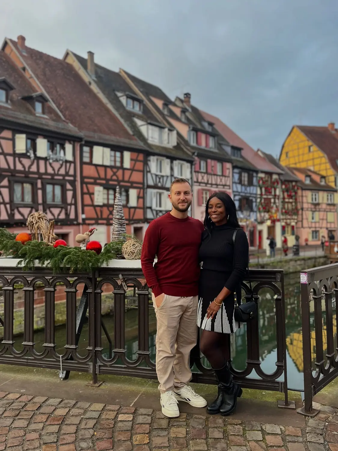 Us on a decorated bridge over the canal in Colmar's Little Venice, colourful timber houses behind