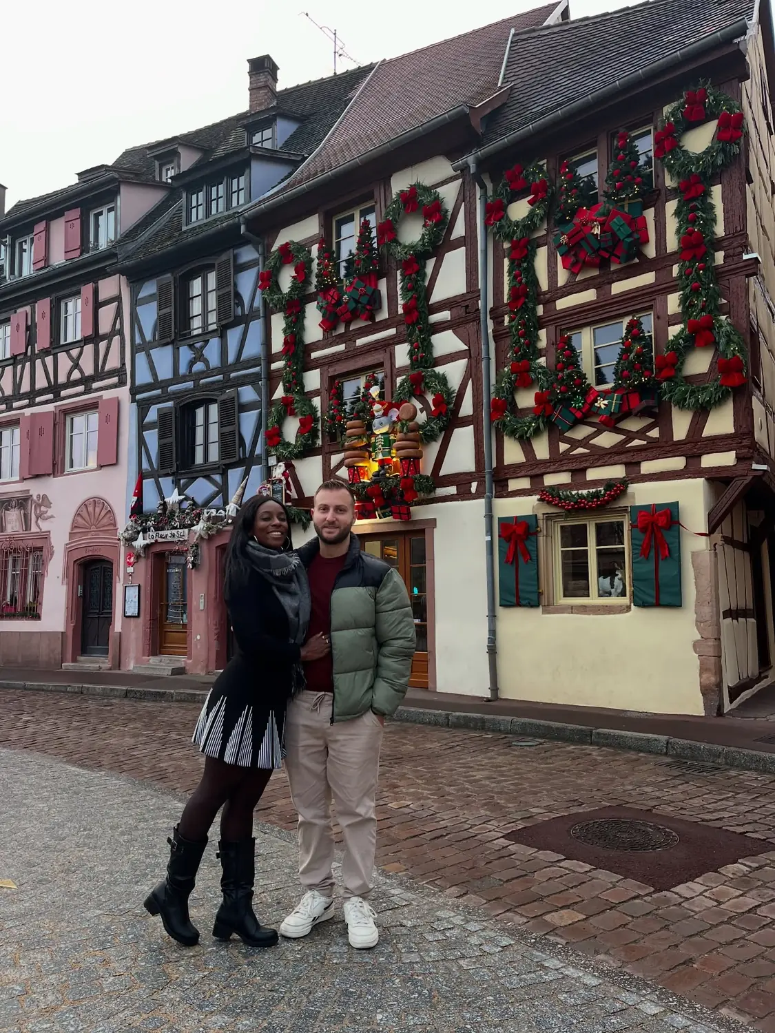 Us in front of a Colmar house decorated with giant wreath letters, gifts and a lit nutcracker