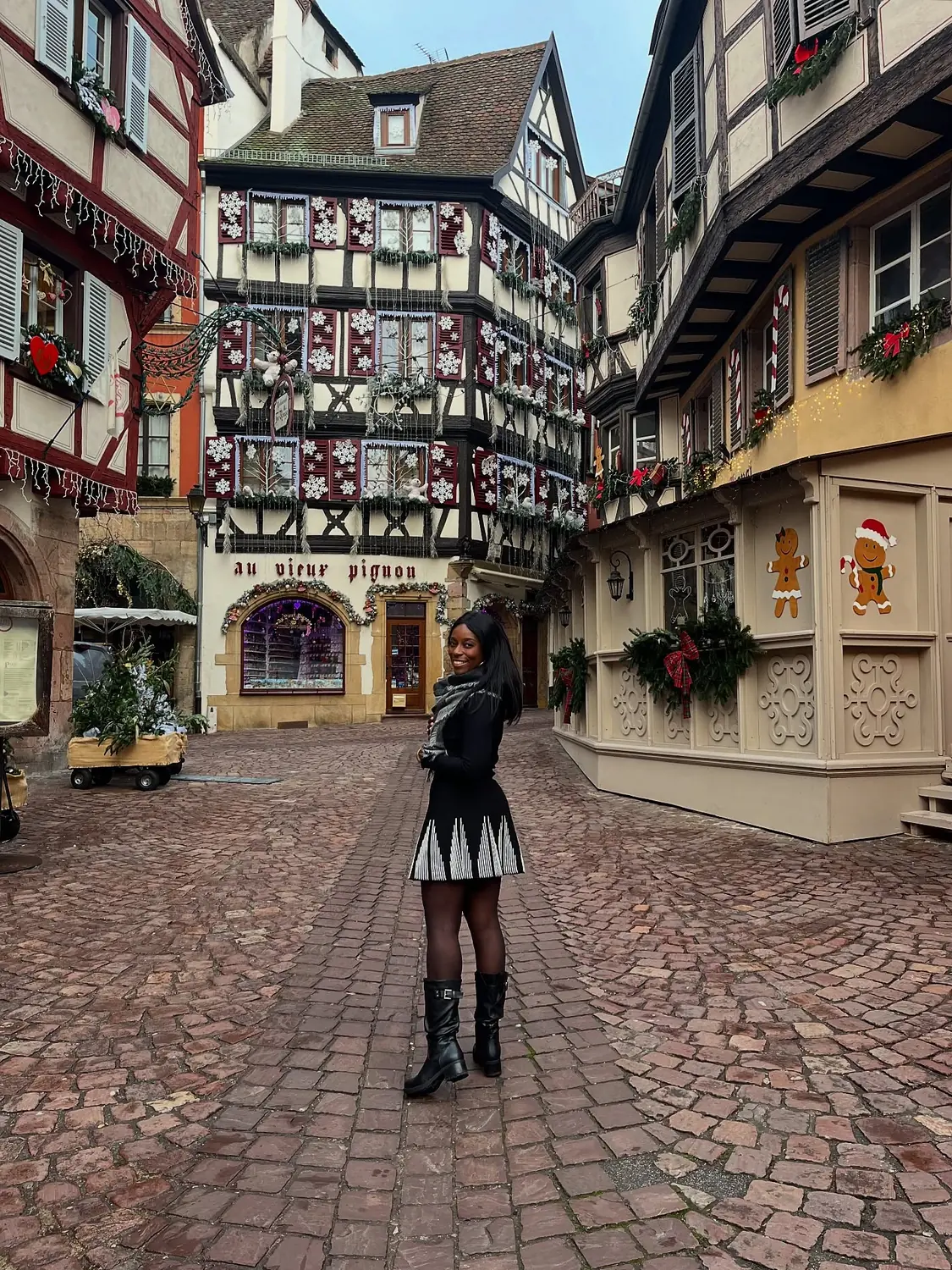 Melody in a cobbled Colmar square in front of the snowflake-covered Au Vieux Pignon house