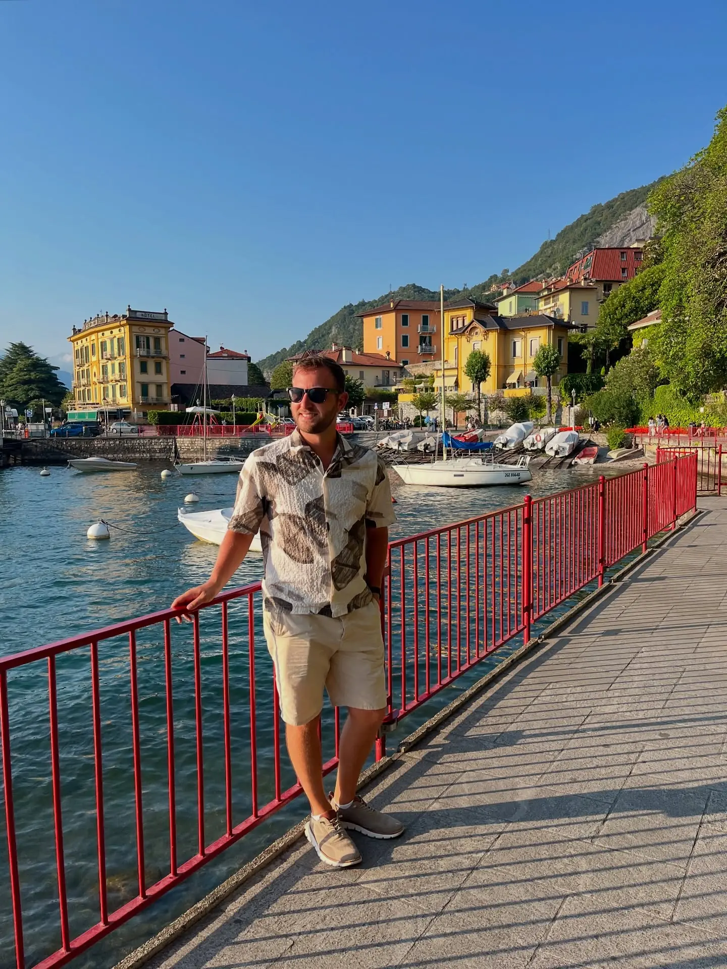 Andrew on Varenna's red-railed harbour promenade with pastel houses