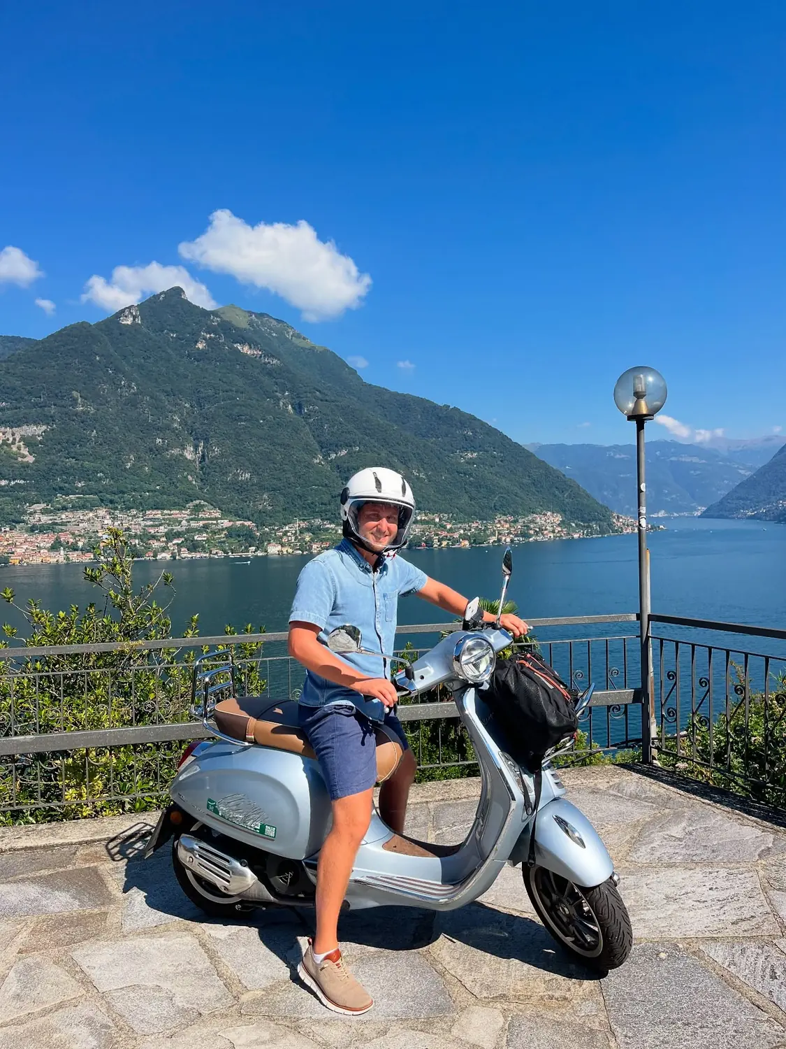 Andrew on a Vespa at a Lake Como viewpoint with the lake and mountains behind