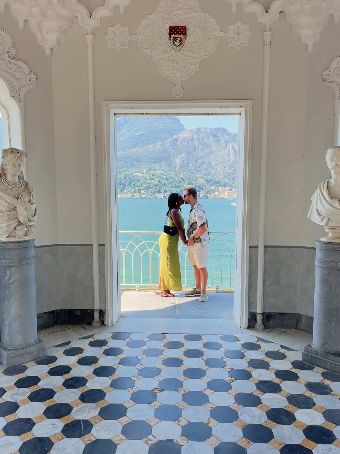 Us kissing in an ornate villa loggia framing the lake, checkerboard marble floor