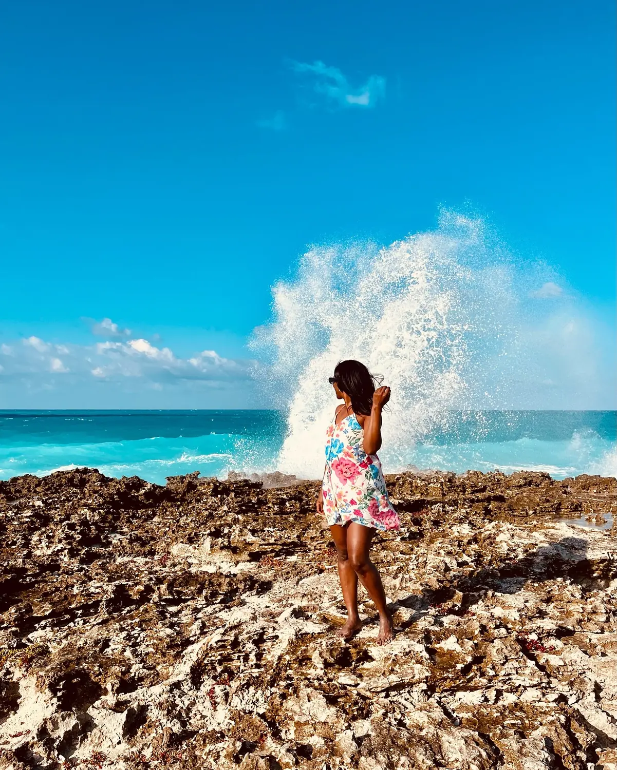 Melody on the rocky east coast as a huge wave explodes on the rocks behind her