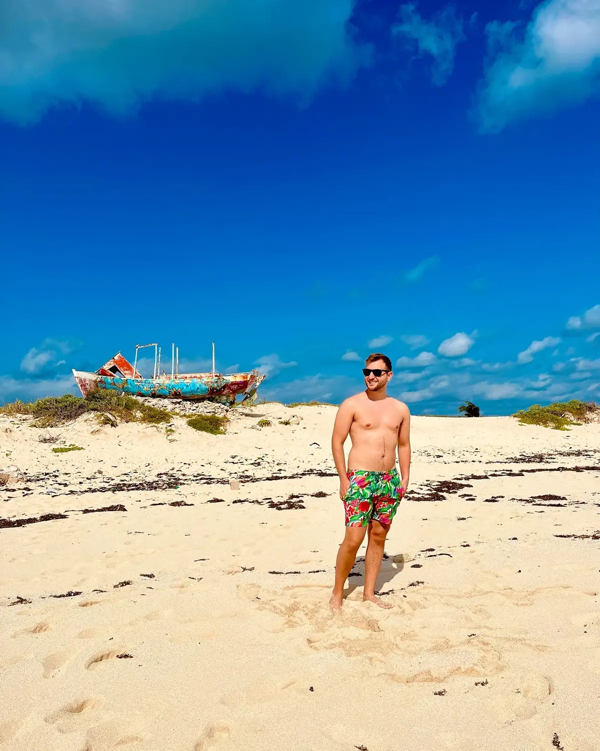 Andrew on a sand dune with the colourful graffiti shipwreck behind