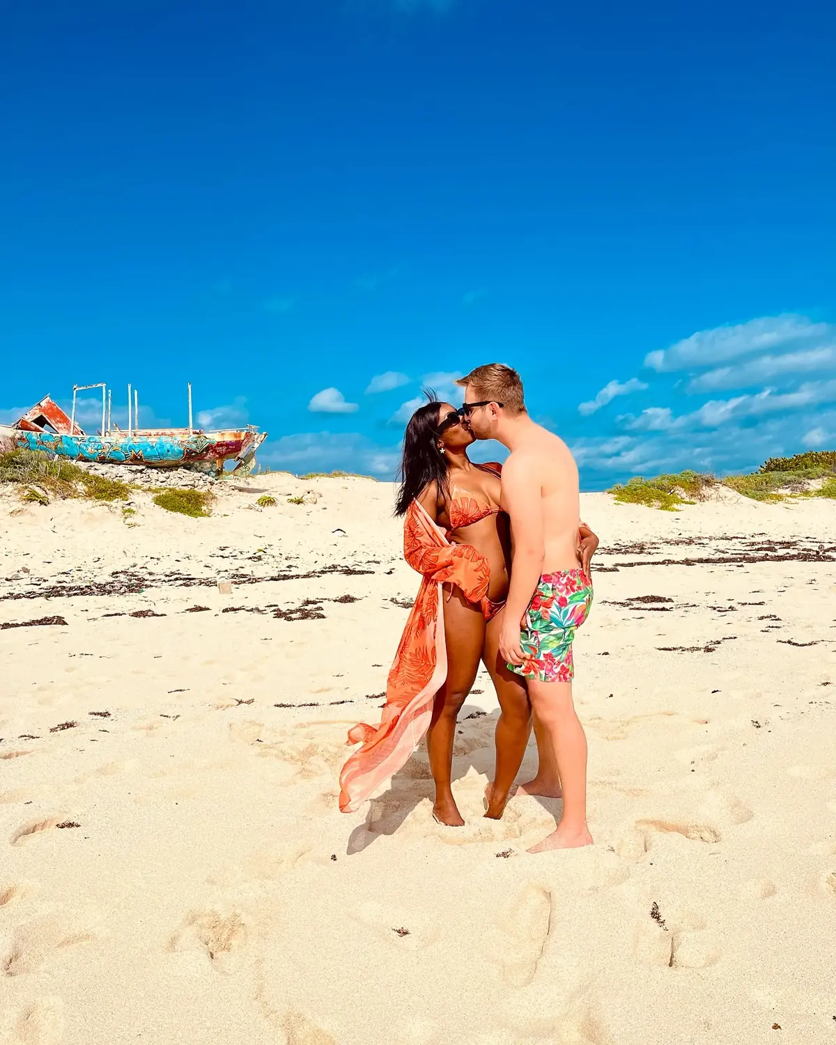 Us kissing on the beach with a graffiti-covered shipwreck behind