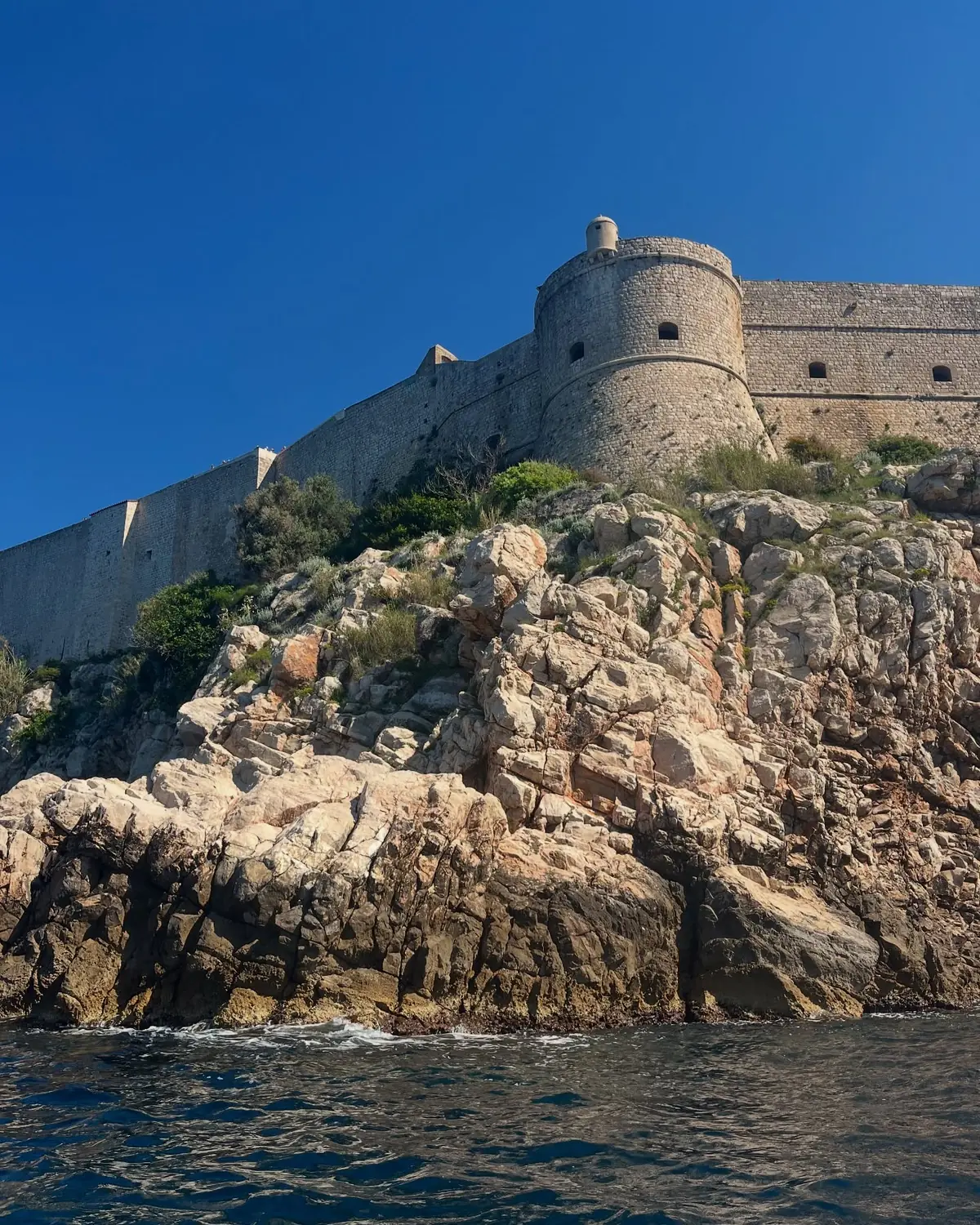 Dubrovnik's massive stone city walls and a round fort rising straight out of the sea cliffs