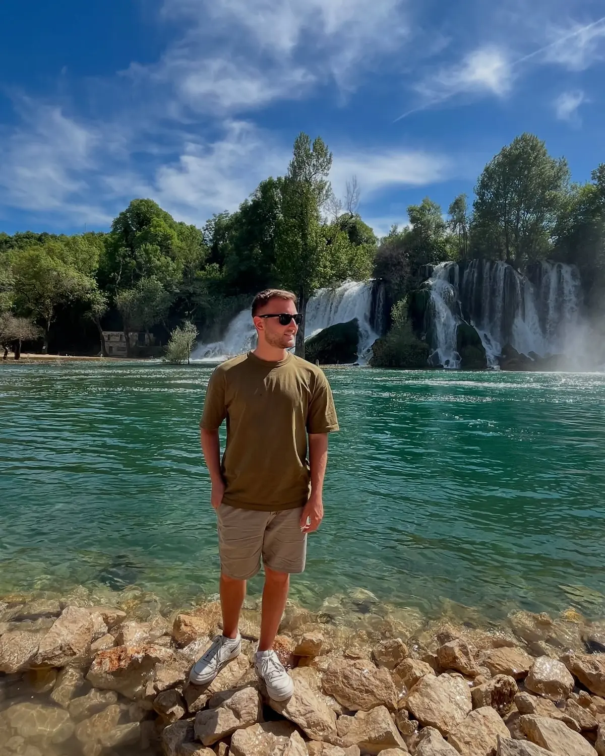Andrew standing on rocks by the emerald pool below the Kravica Waterfalls
