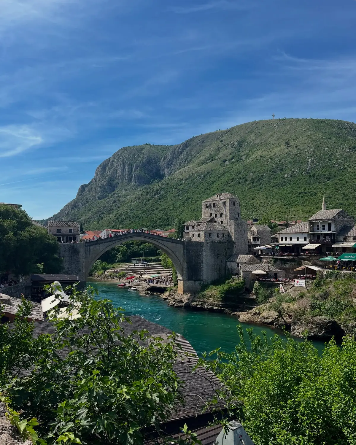 The single stone arch of Mostar's Old Bridge over the turquoise Neretva river, old town and green mountain behind