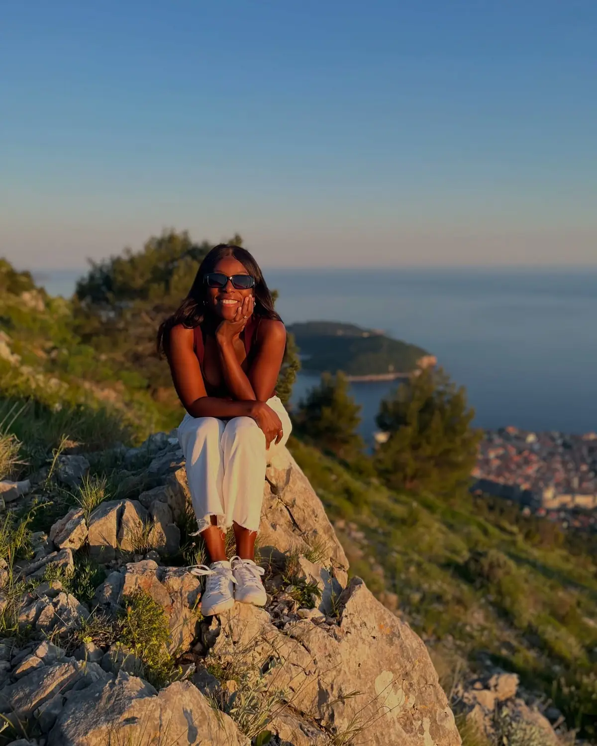 Andrew sitting on a rock high above Dubrovnik's Old Town and harbour in warm evening light
