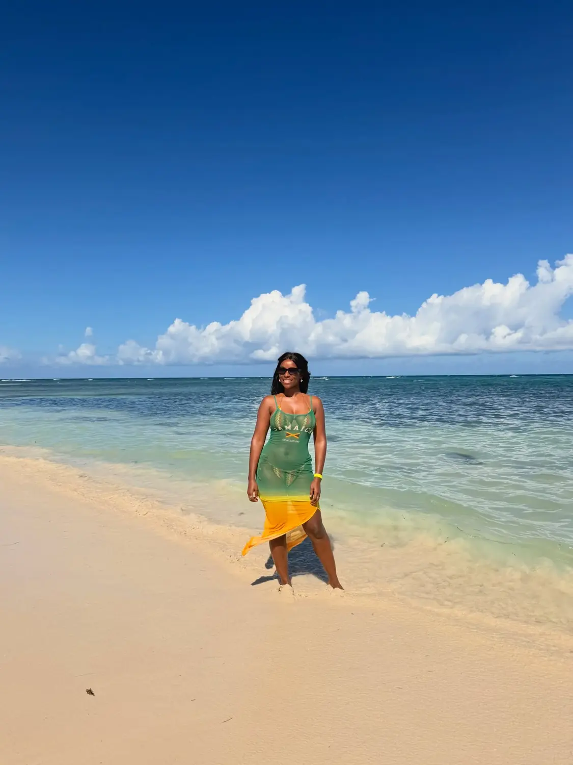 Melody in a green-and-gold Jamaica dress on a bright Falmouth beach