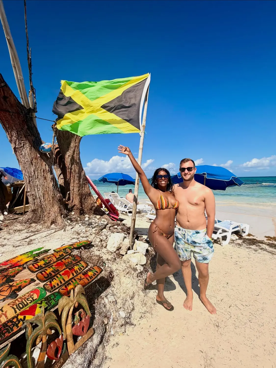 Us on a Jamaican beach beneath a waving Jamaican flag near Falmouth