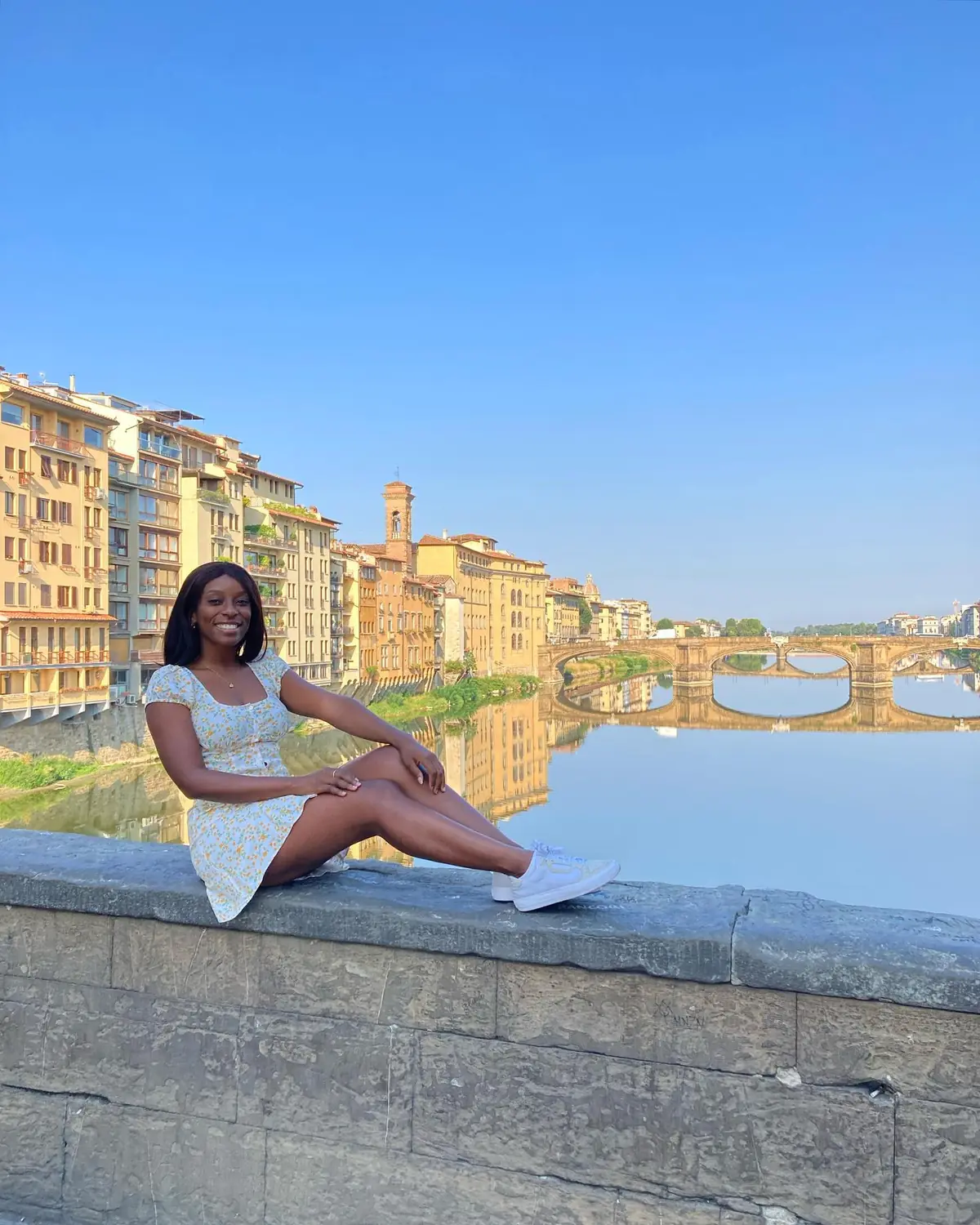 Melody sitting on a wall above the Arno with bridges reflected in the water