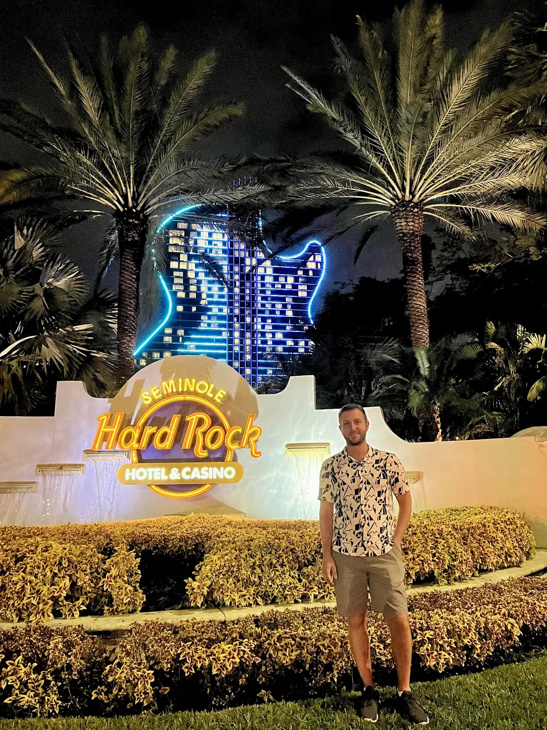 Andrew by the lit Hard Rock Hotel sign and palm trees at night