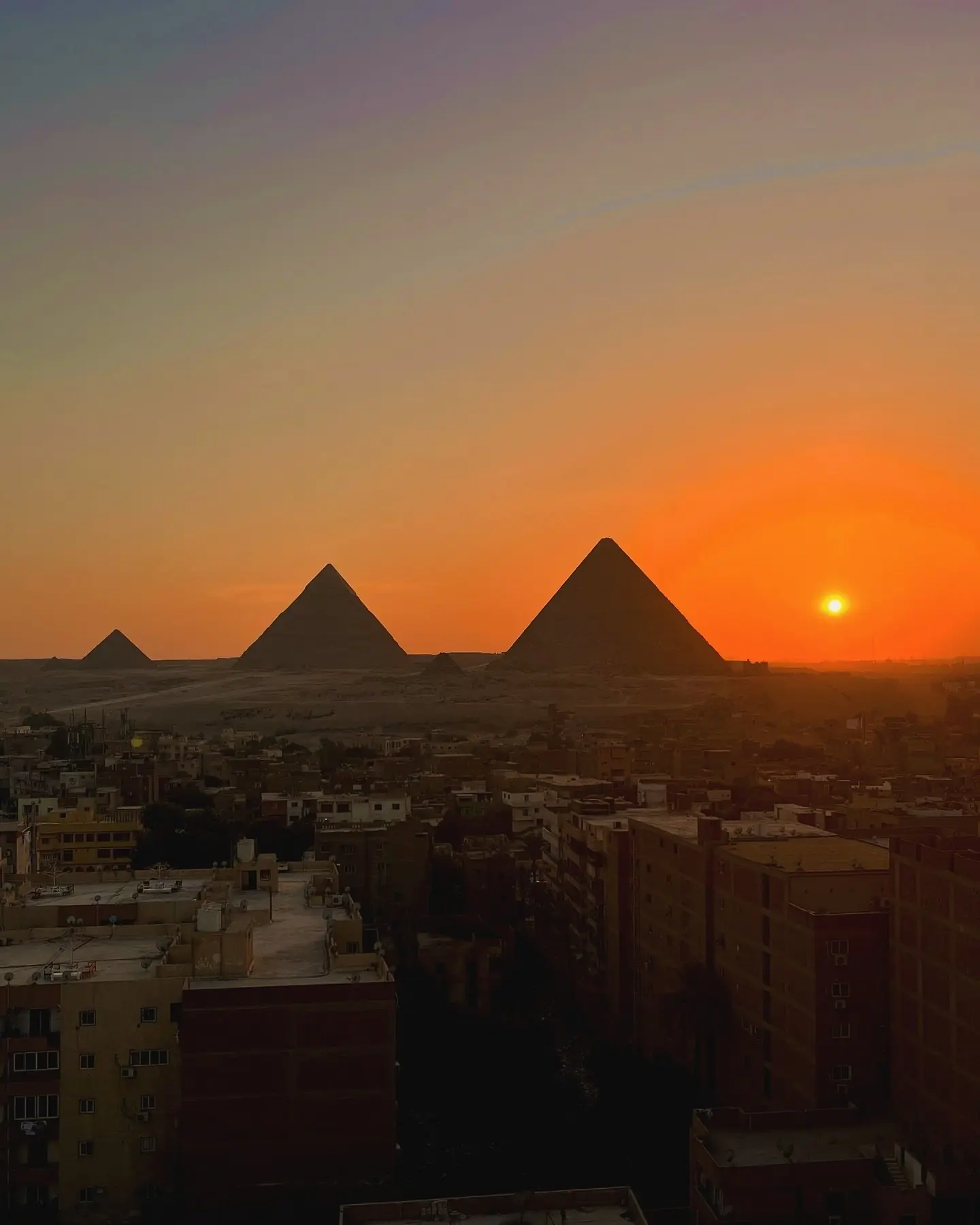 Sun setting behind the Giza pyramids over the rooftops of the city