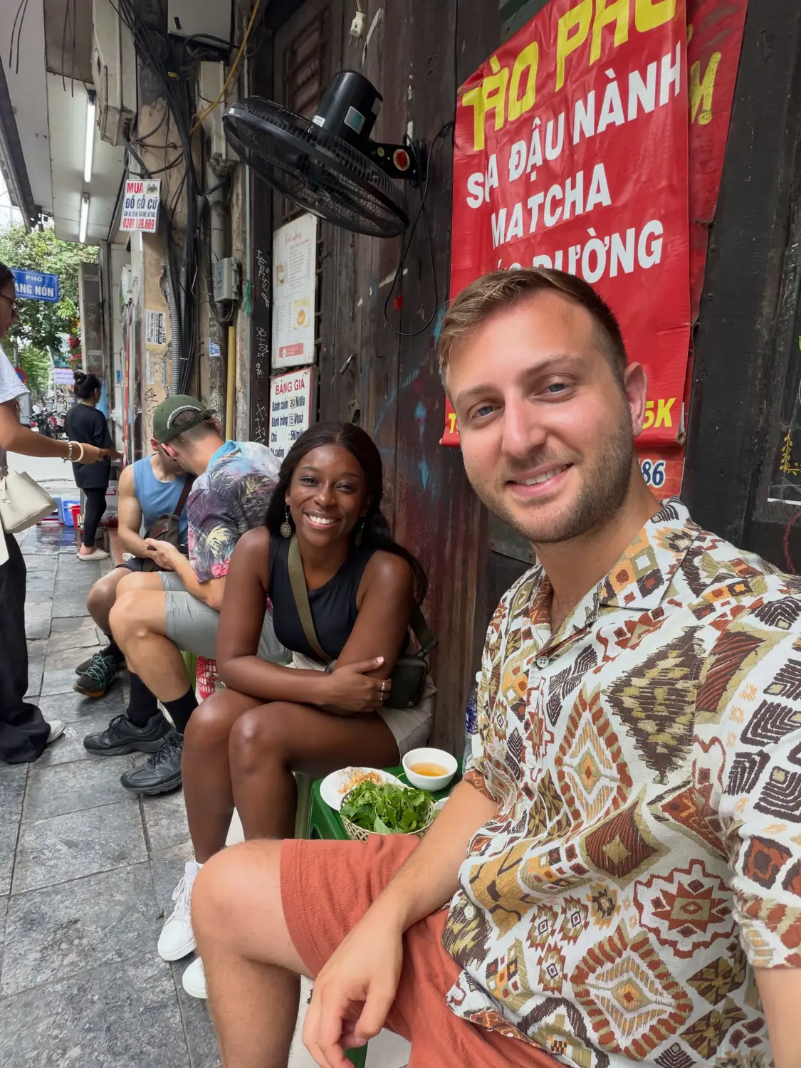 Us perched on little plastic stools eating street food in the Old Quarter