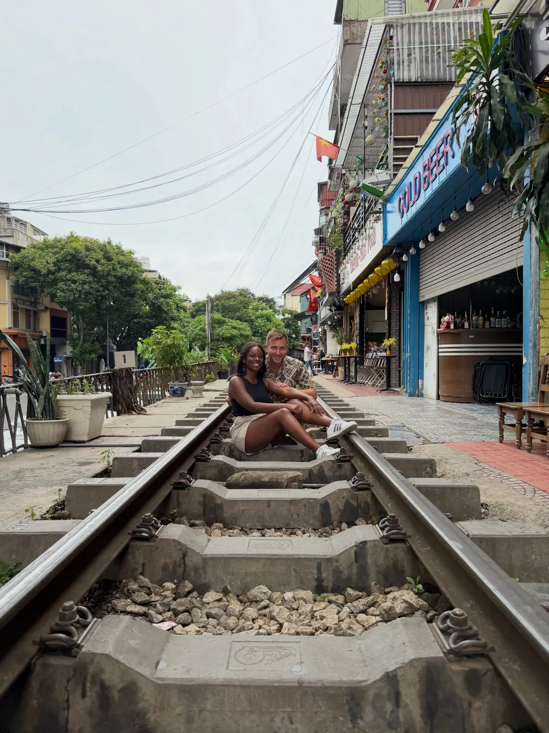 Us sitting together on the tracks of Hanoi Train Street, lanterns and cafés glowing behind