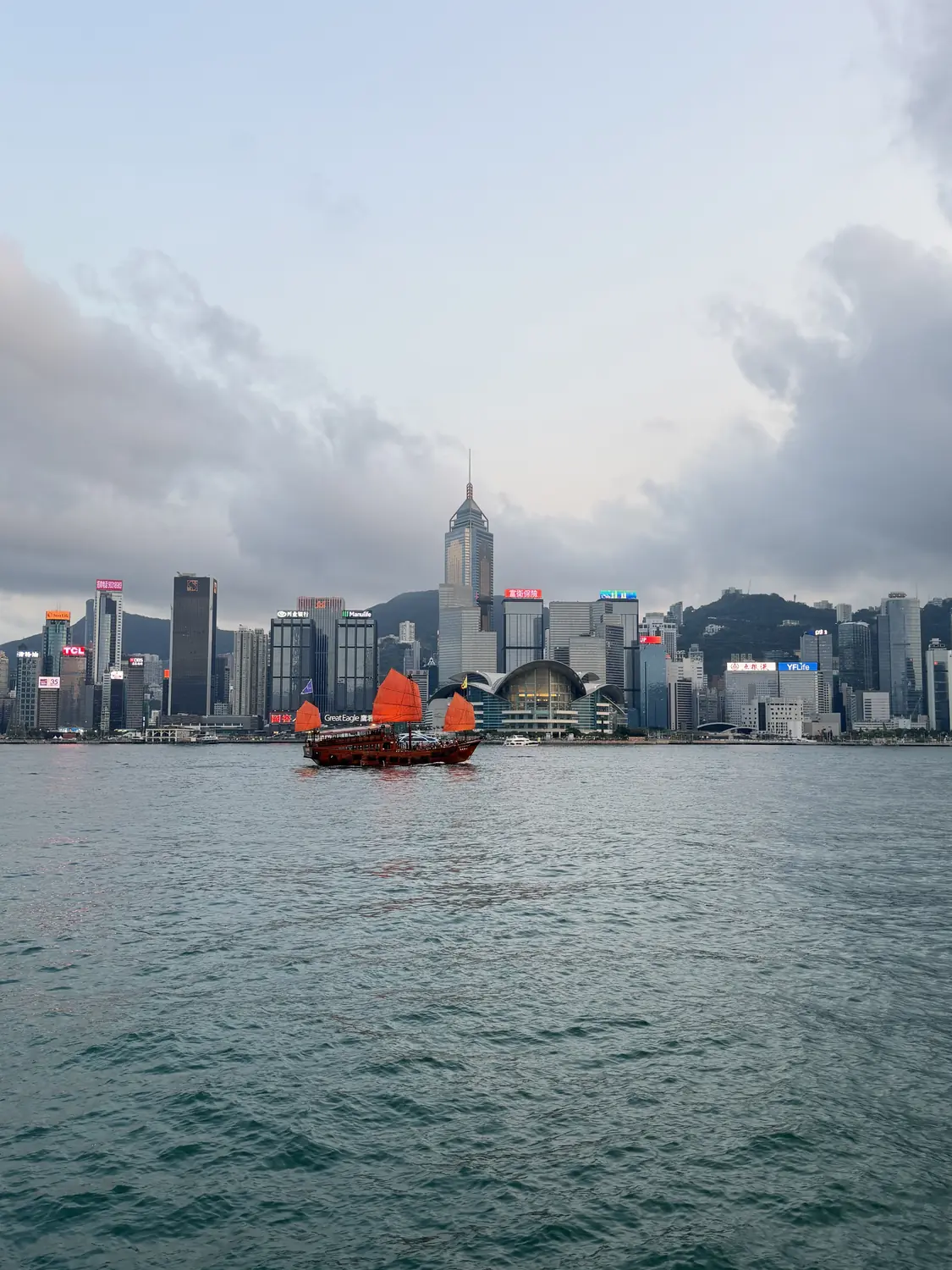 Victoria Harbour by day with the Hong Kong skyline and a red Chinese junk boat
