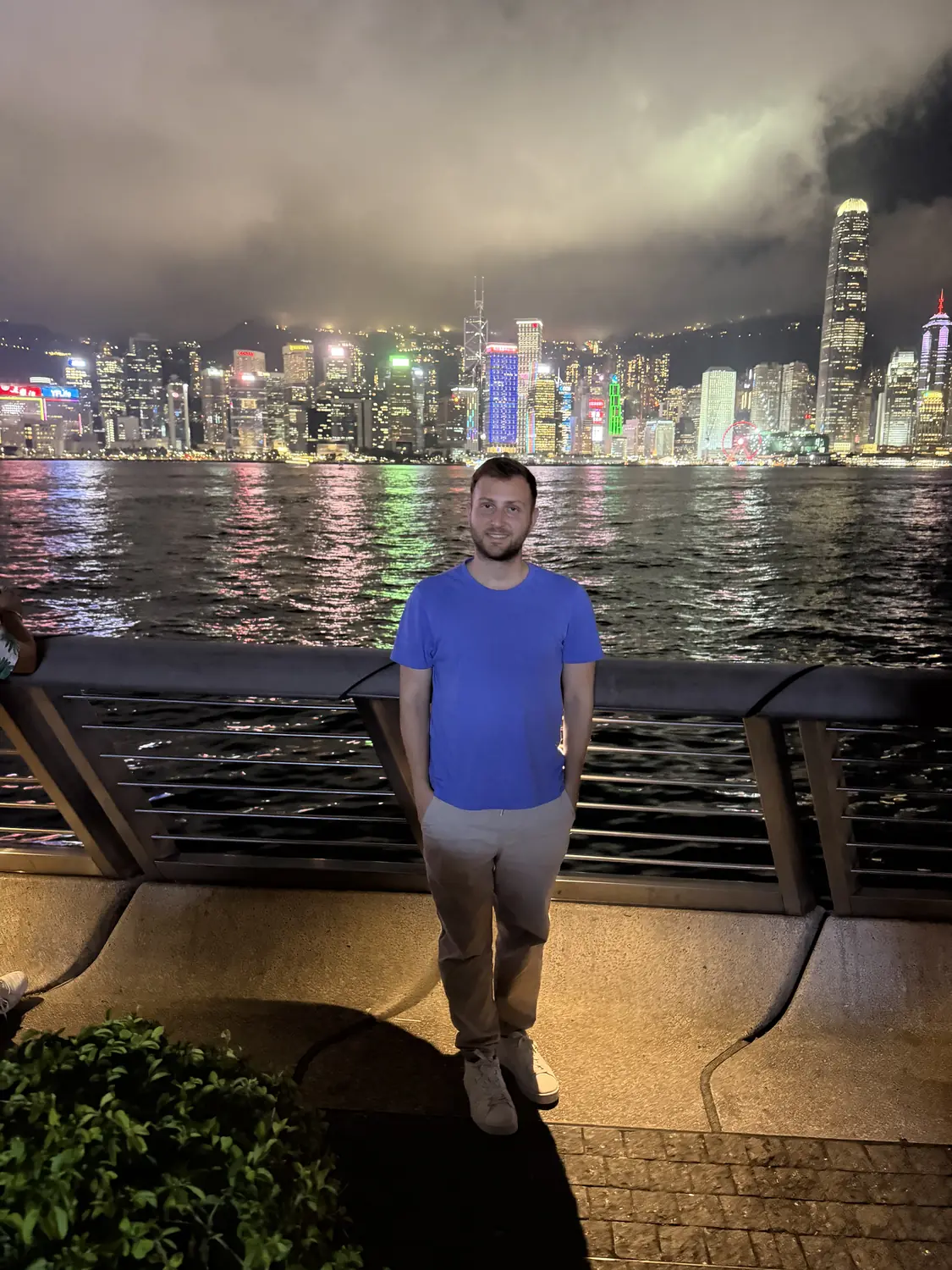 Andrew on the Tsim Sha Tsui promenade at night with the lit Hong Kong skyline behind