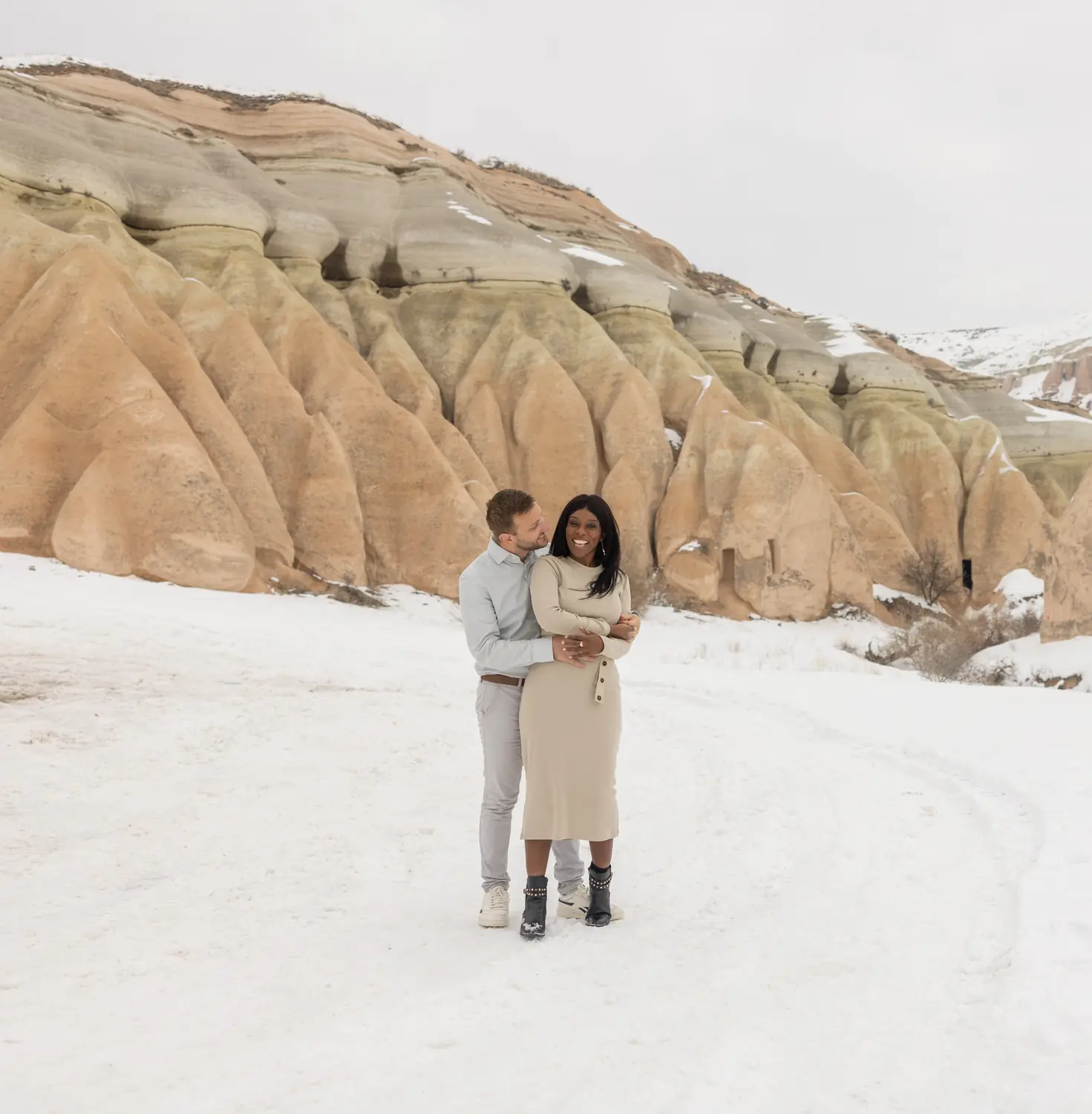 Andrew and Melody embracing in the snow beneath the rose-coloured rock formations of Cappadocia, Turkey