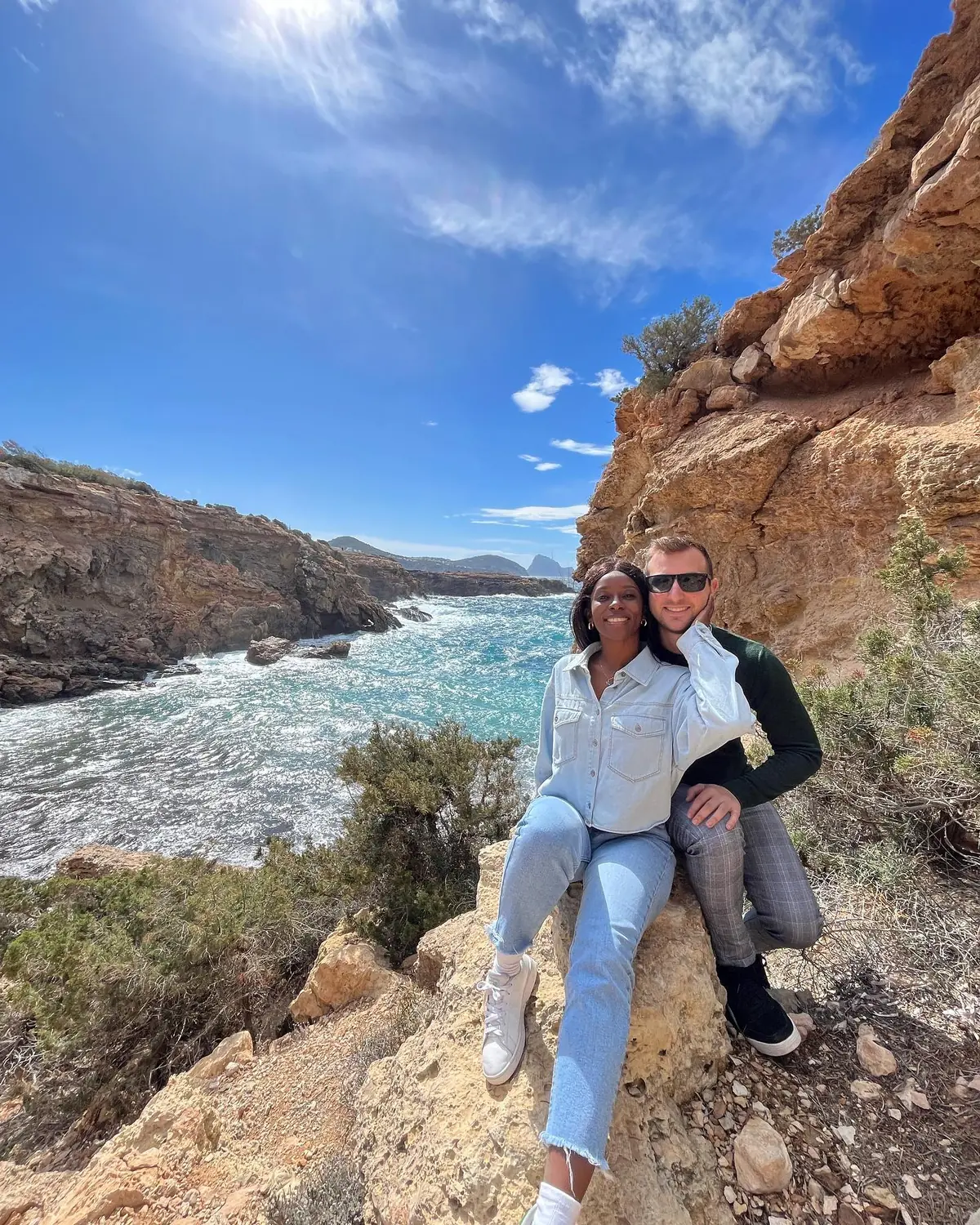 Us sitting on a rock ledge above a churning turquoise inlet on Ibiza