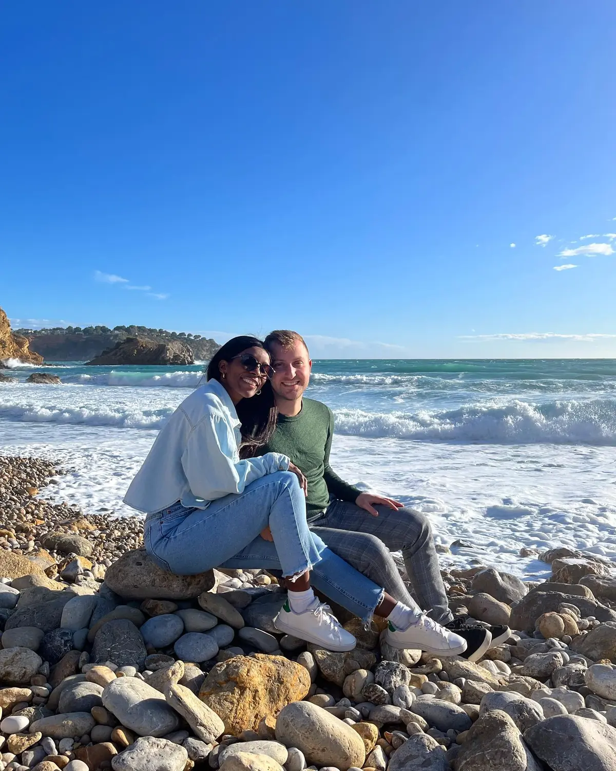 Us sitting together on a pebble beach as the waves roll in on Ibiza