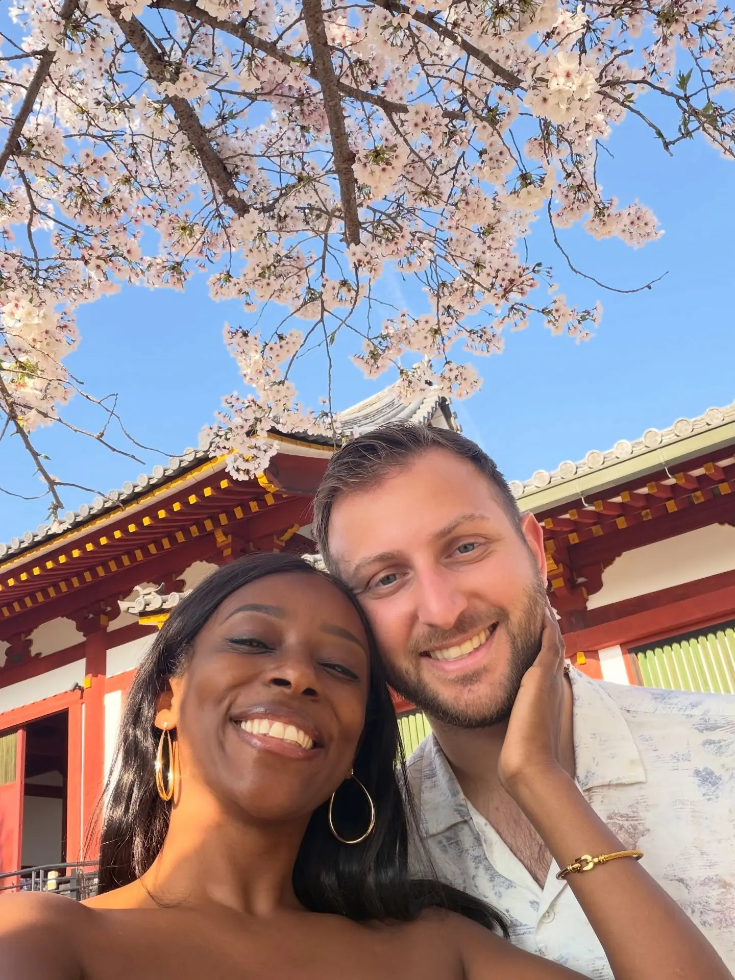 A selfie under blossoms by a vermilion temple