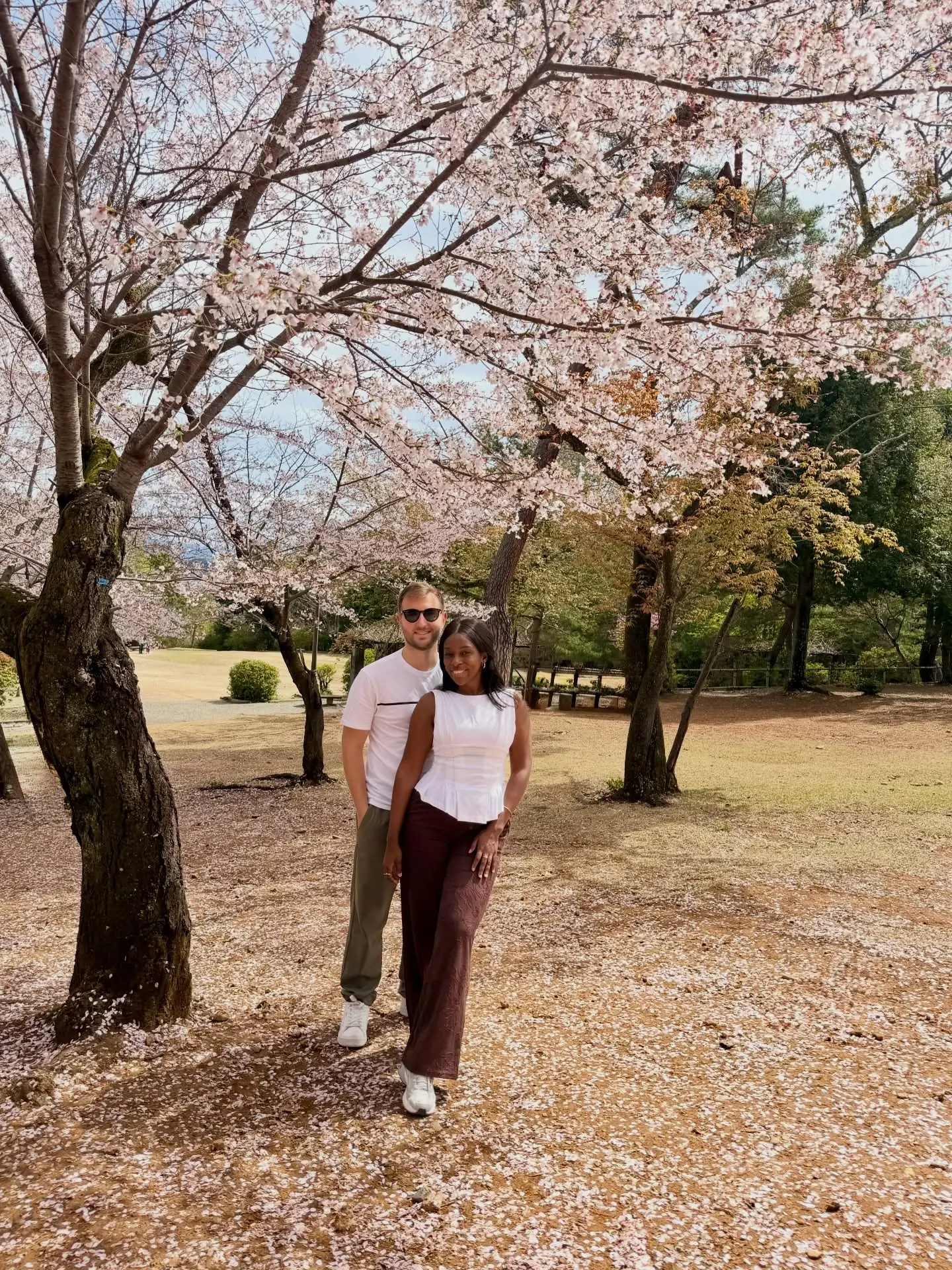 Us under cherry trees with fallen petals across a Kyoto park