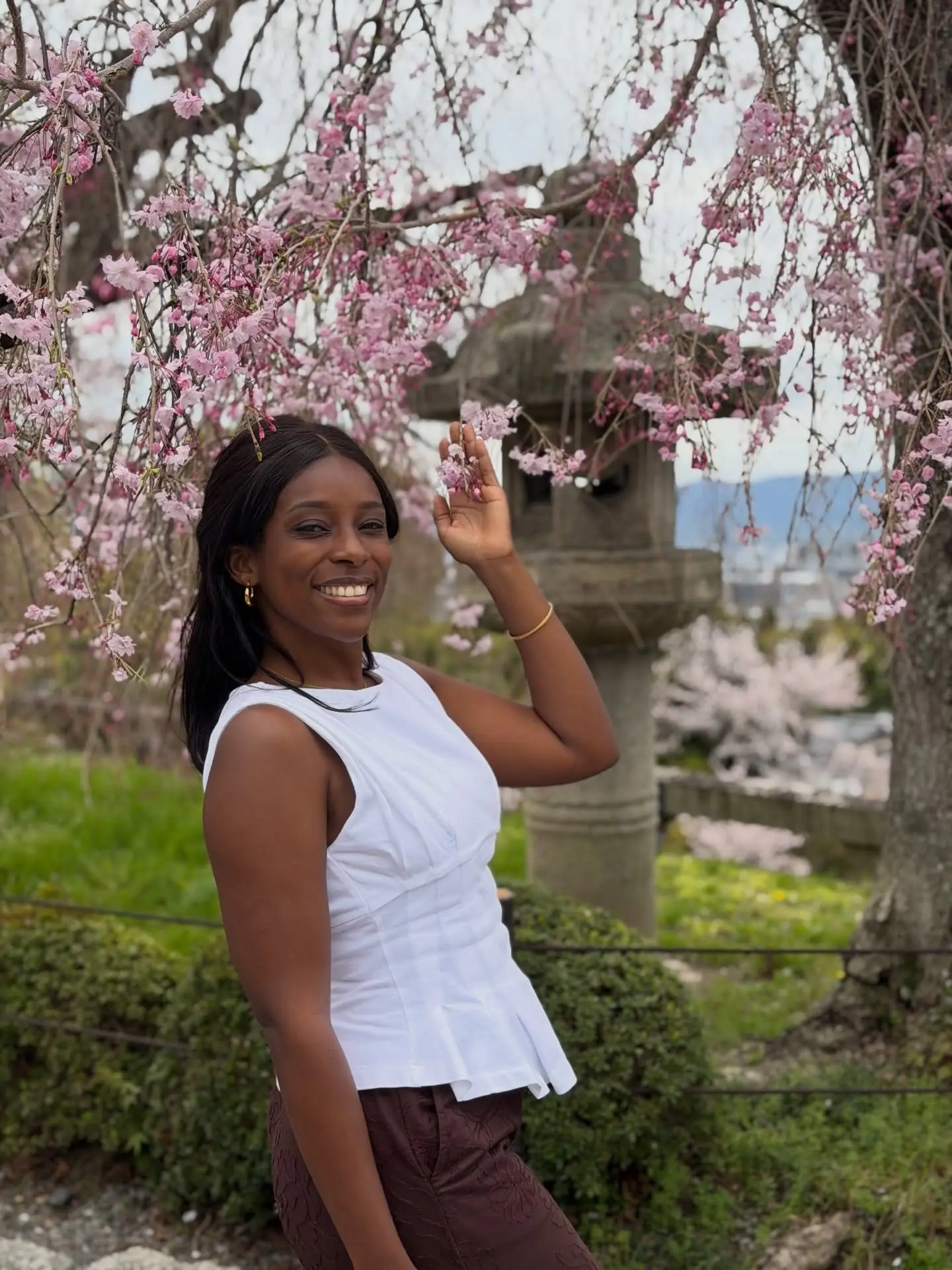 Melody beneath weeping pink cherry blossoms by a stone lantern in Kyoto