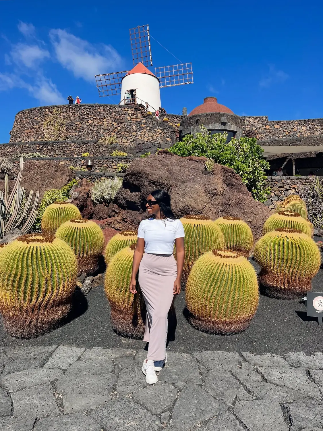 Melody in front of rows of giant round barrel cacti with a white windmill above at the Jardín de Cactus