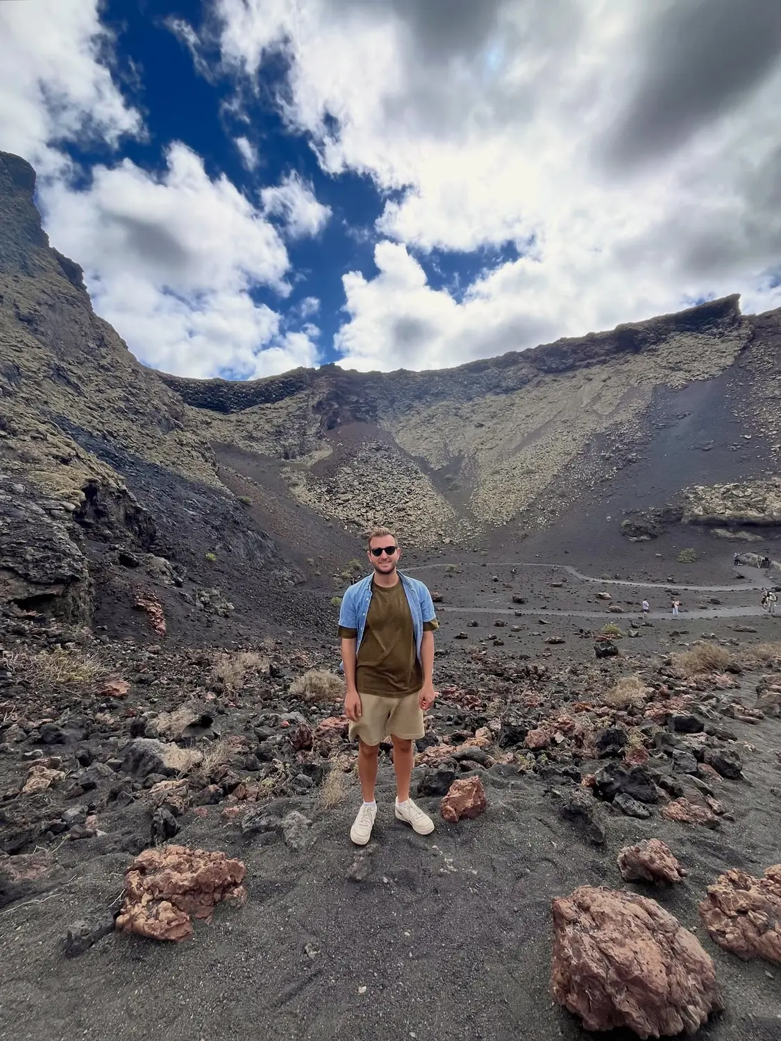 Andrew standing inside a volcanic crater surrounded by red lava rock in Timanfaya